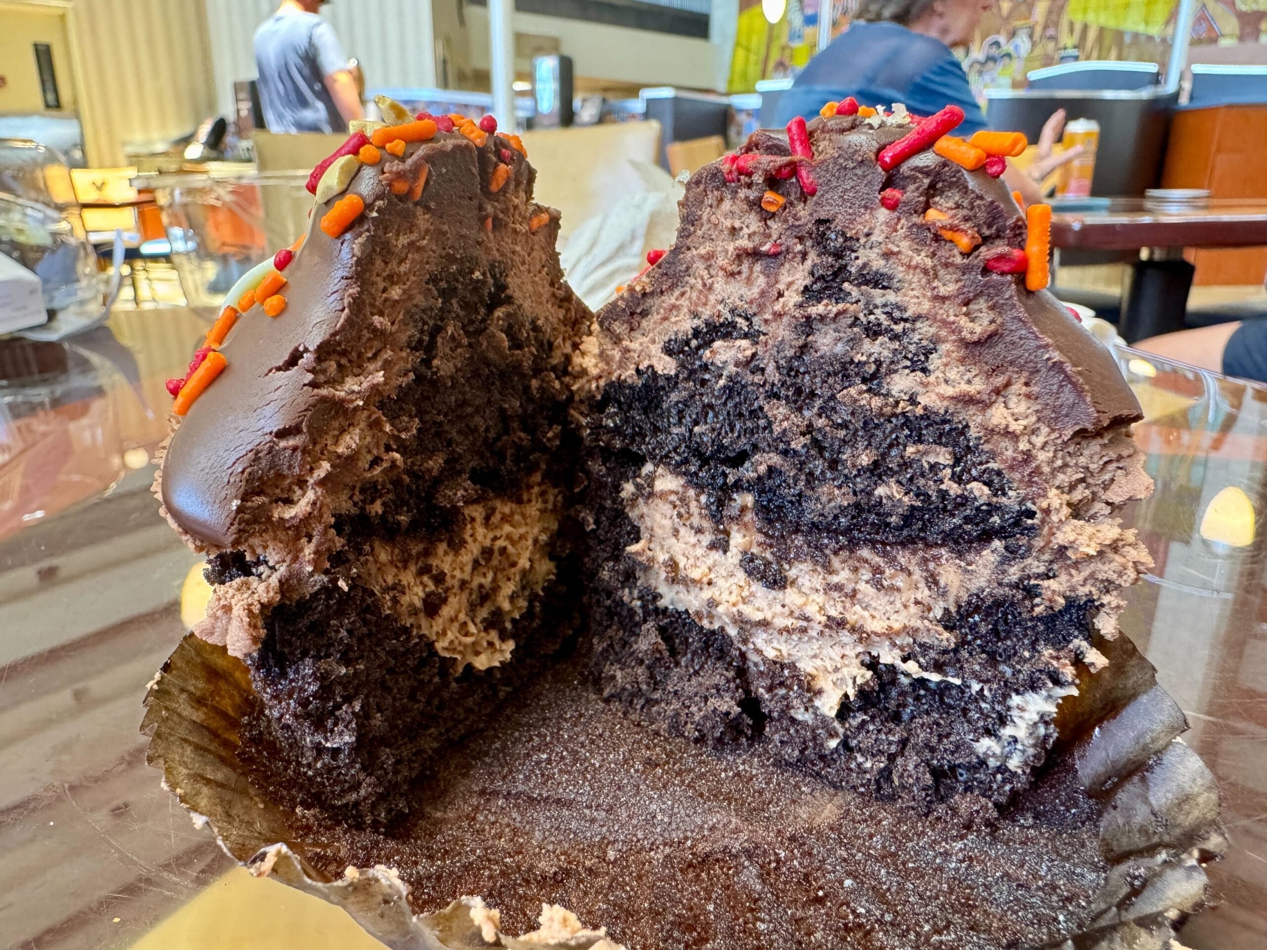 A large chocolate cupcake with sprinkles and creamy filling sits on a table at Contempo Cafe, tempting dessert lovers.