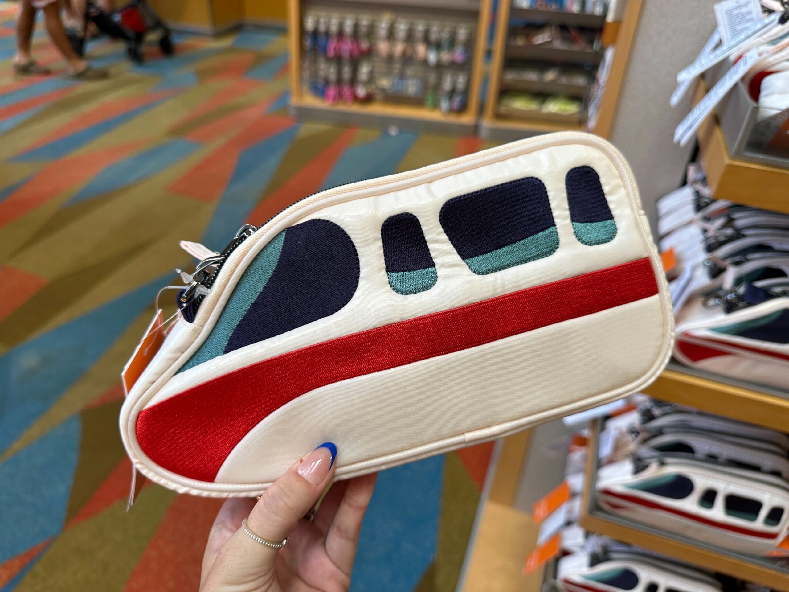 A hand holds a pouch designed to look like a monorail, with red, black, and teal accents.