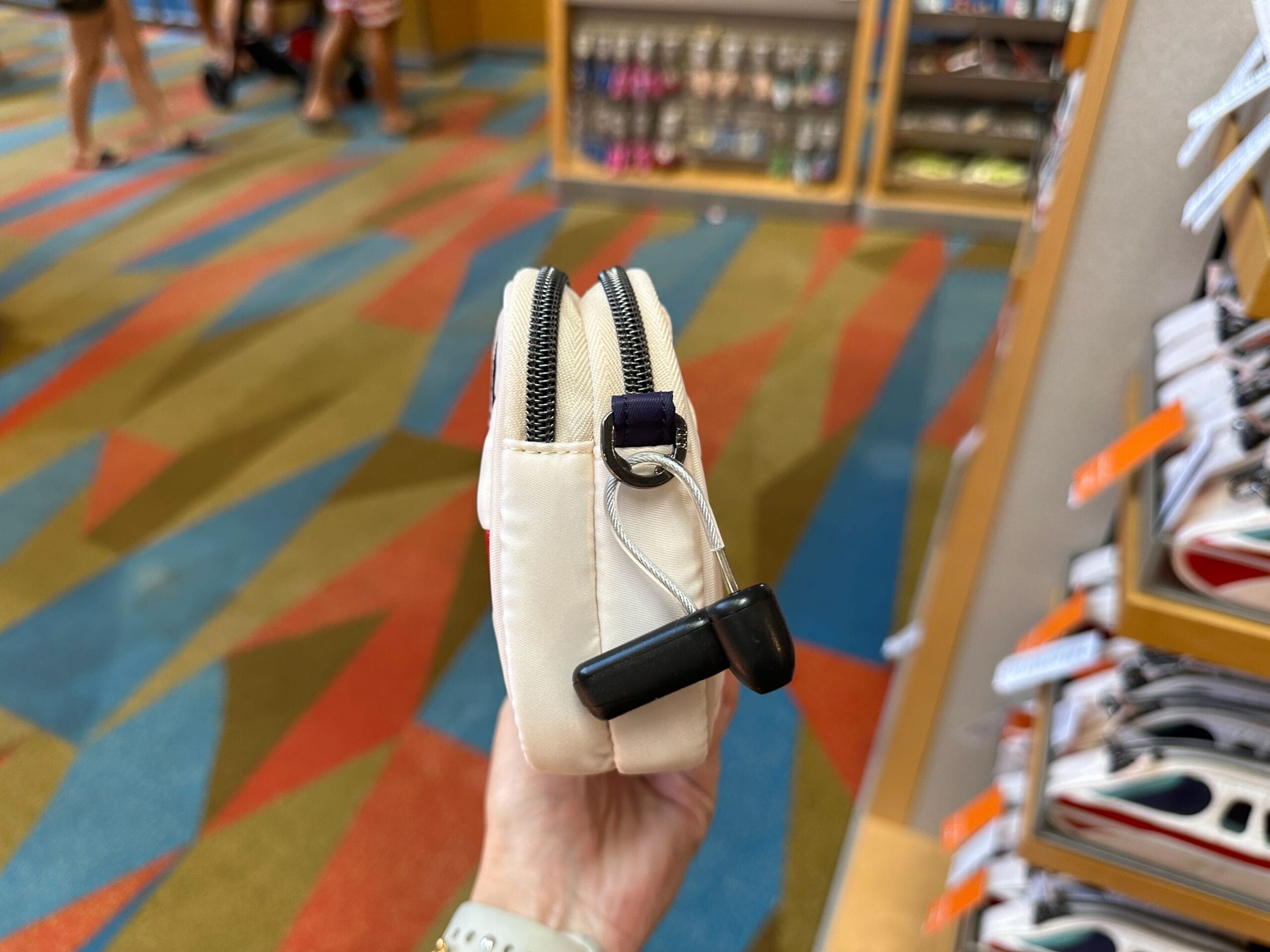 A hand holds a small, zippered beige pouch with a security tag in a colorful store aisle.