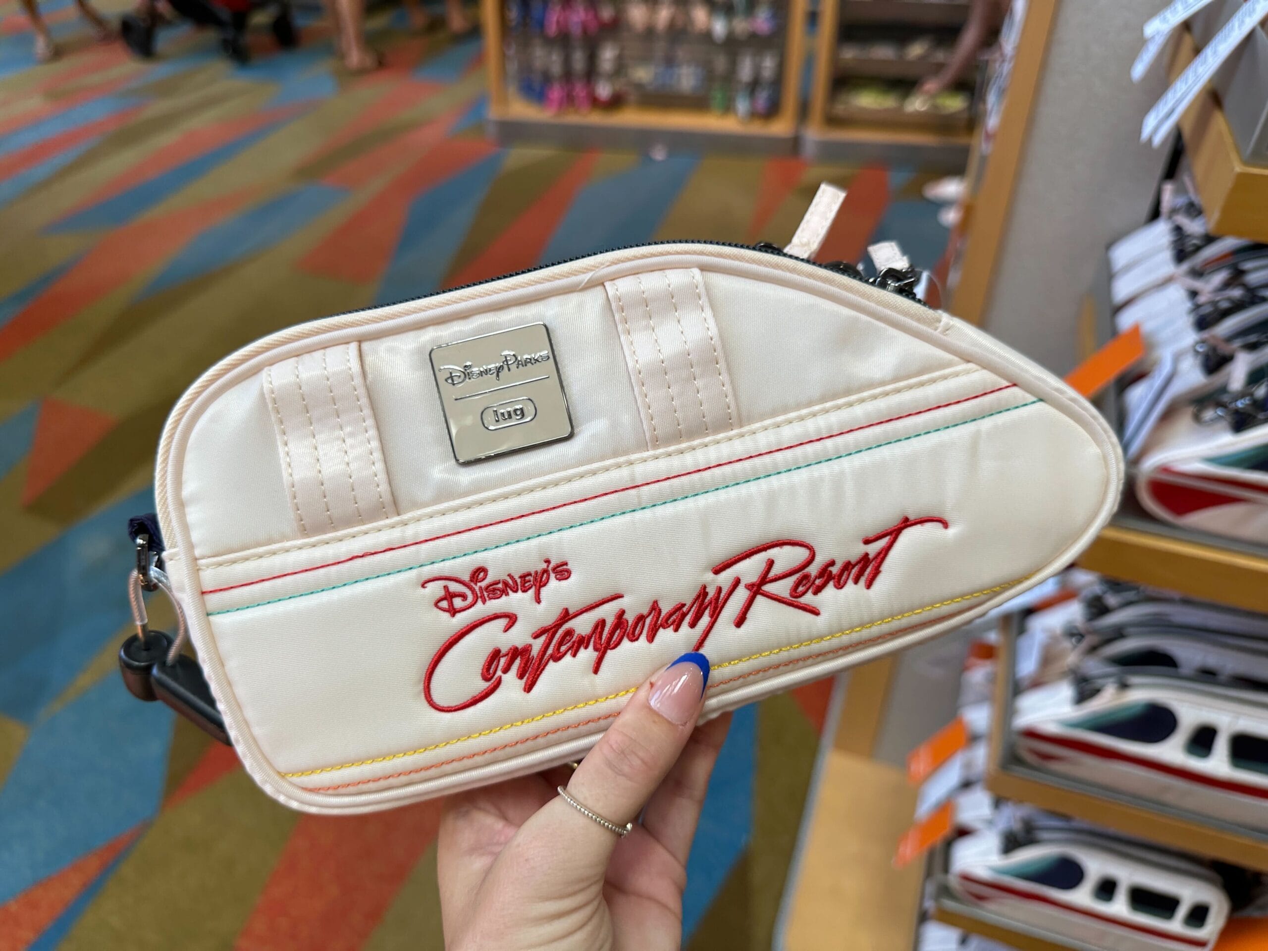 Cream-colored bag with "Disney's Contemporary Resort" logo, held in a store with colorful carpet.