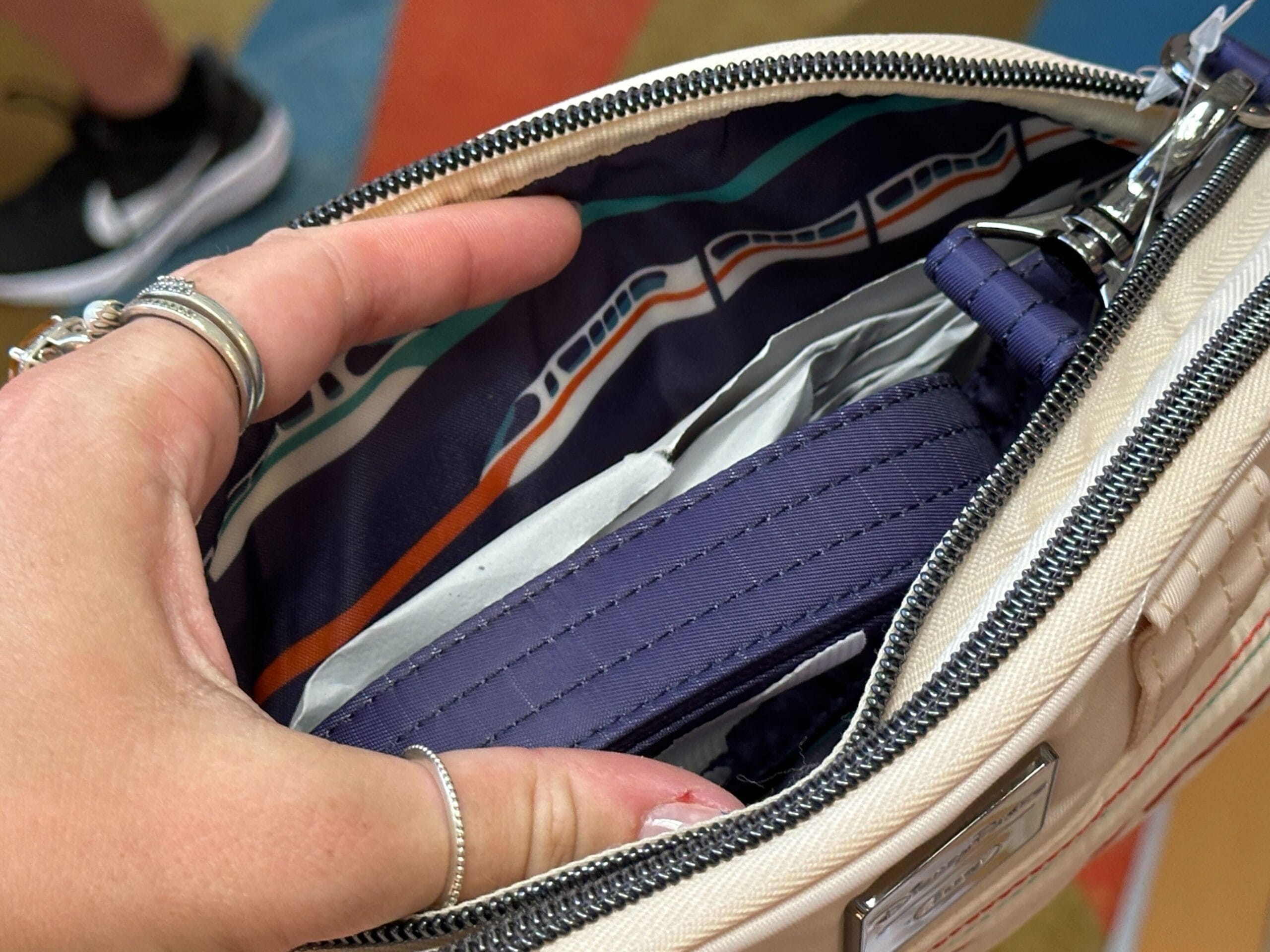 A hand holds open a purse, showing a blue wallet and a colorful pattern with trains inside the lining.