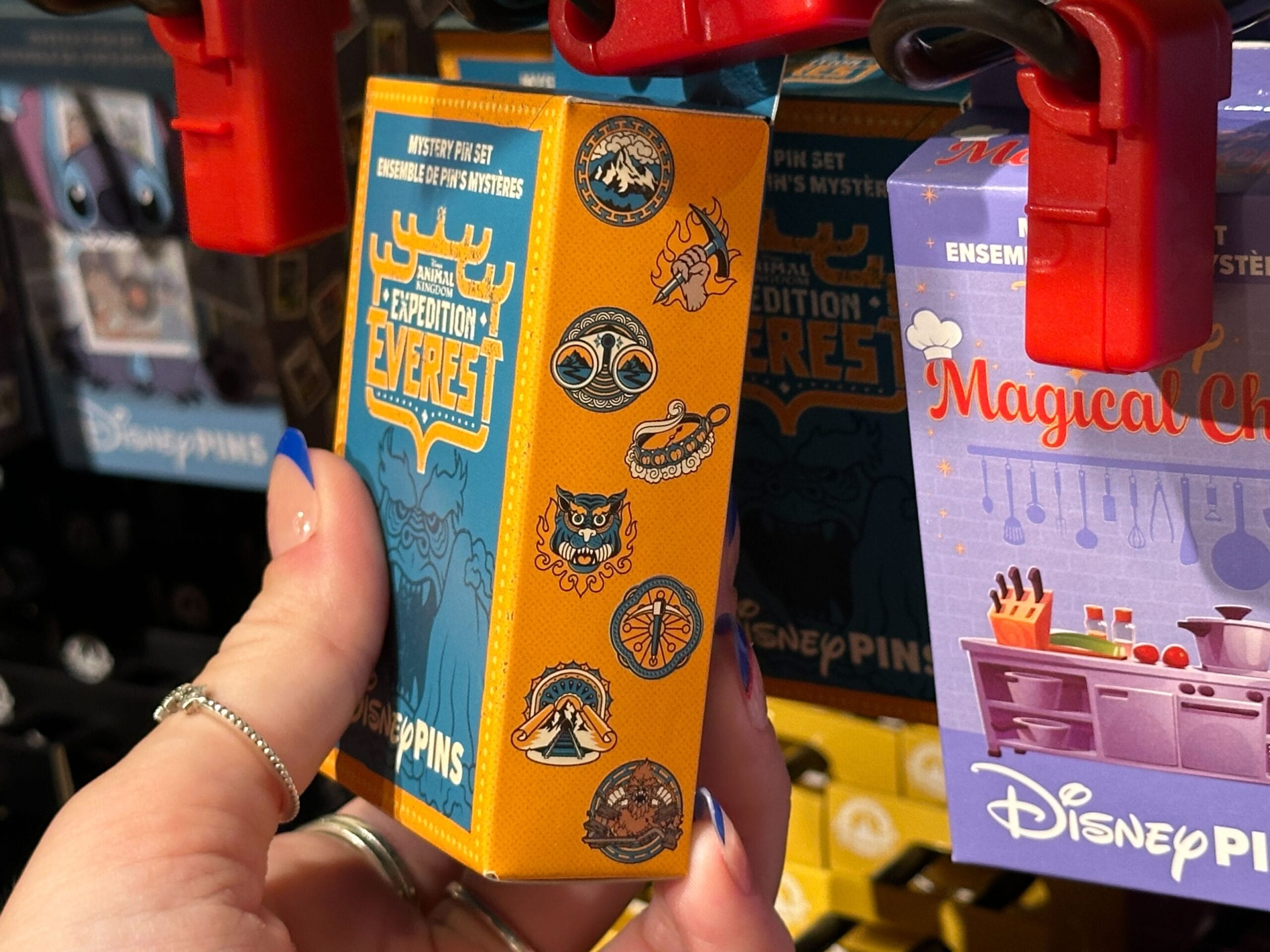 Close-up of a hand holding an orange Expedition Everest Disney pin box decorated with themed icons and designs.