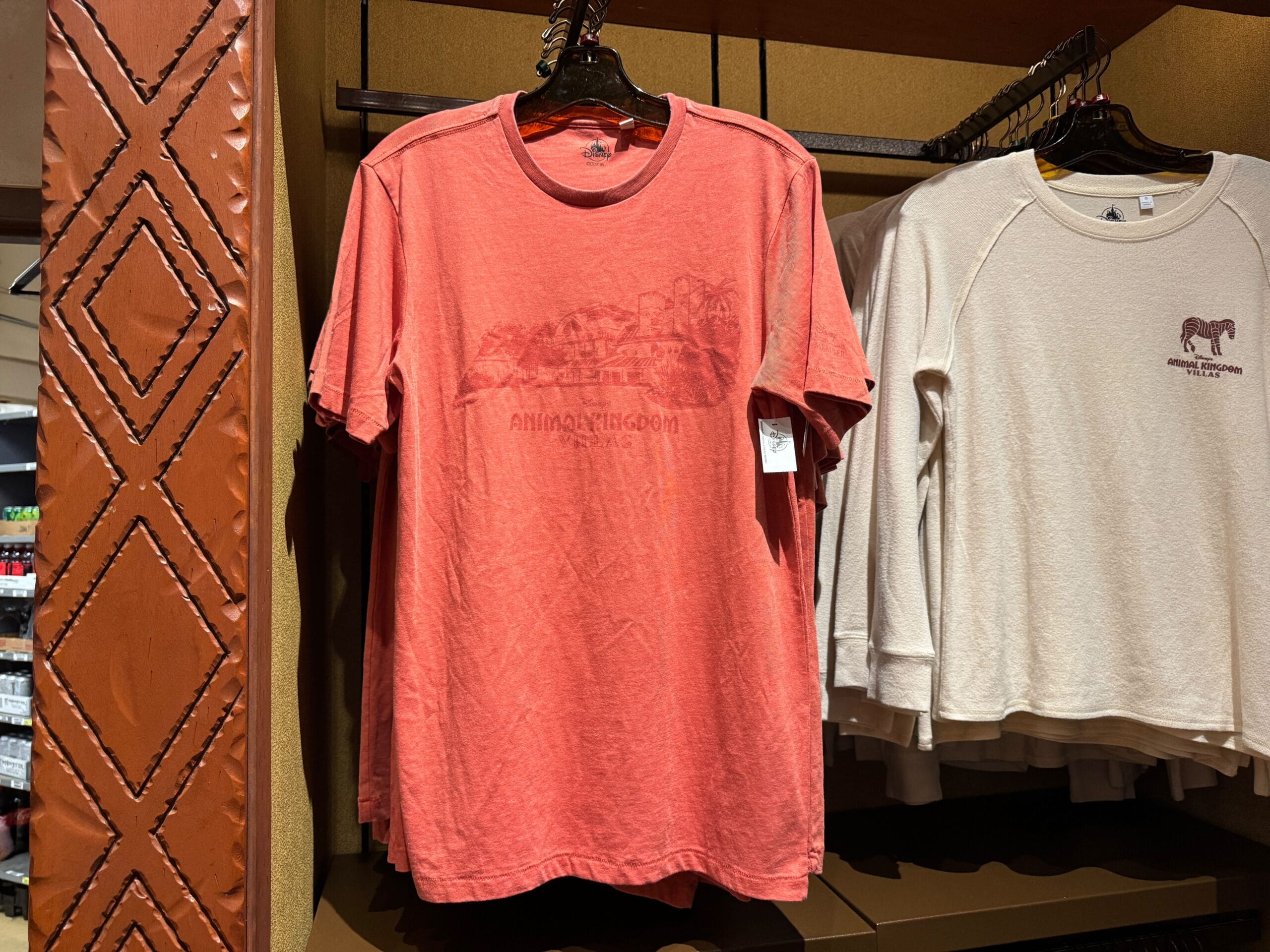 A coral-colored Animal Kingdom t-shirt on a rack next to a beige shirt with an animal graphic.