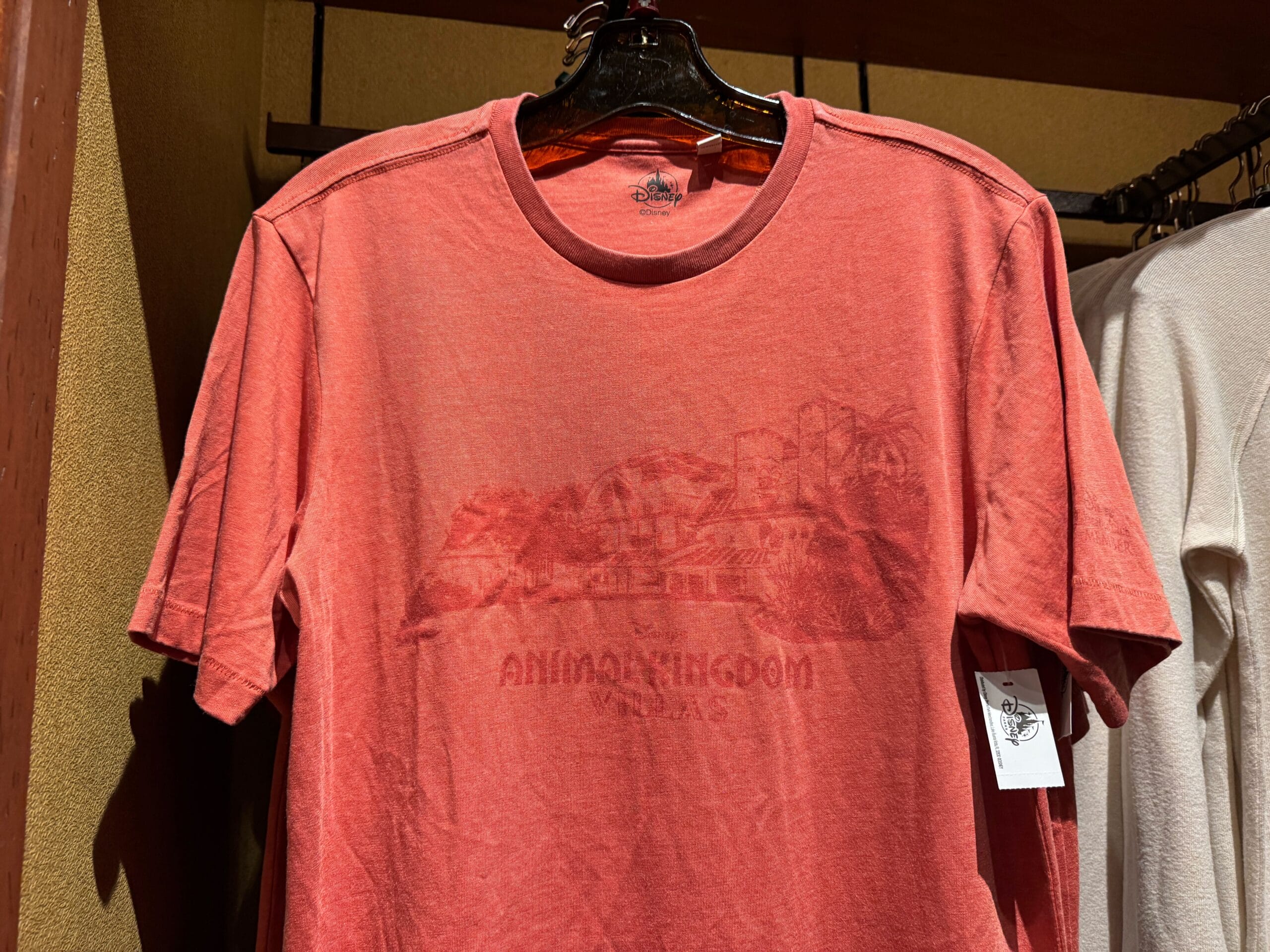Red t-shirt on hanger with a faint Animal Kingdom lodge graphic and text across the chest, displayed in a store.
