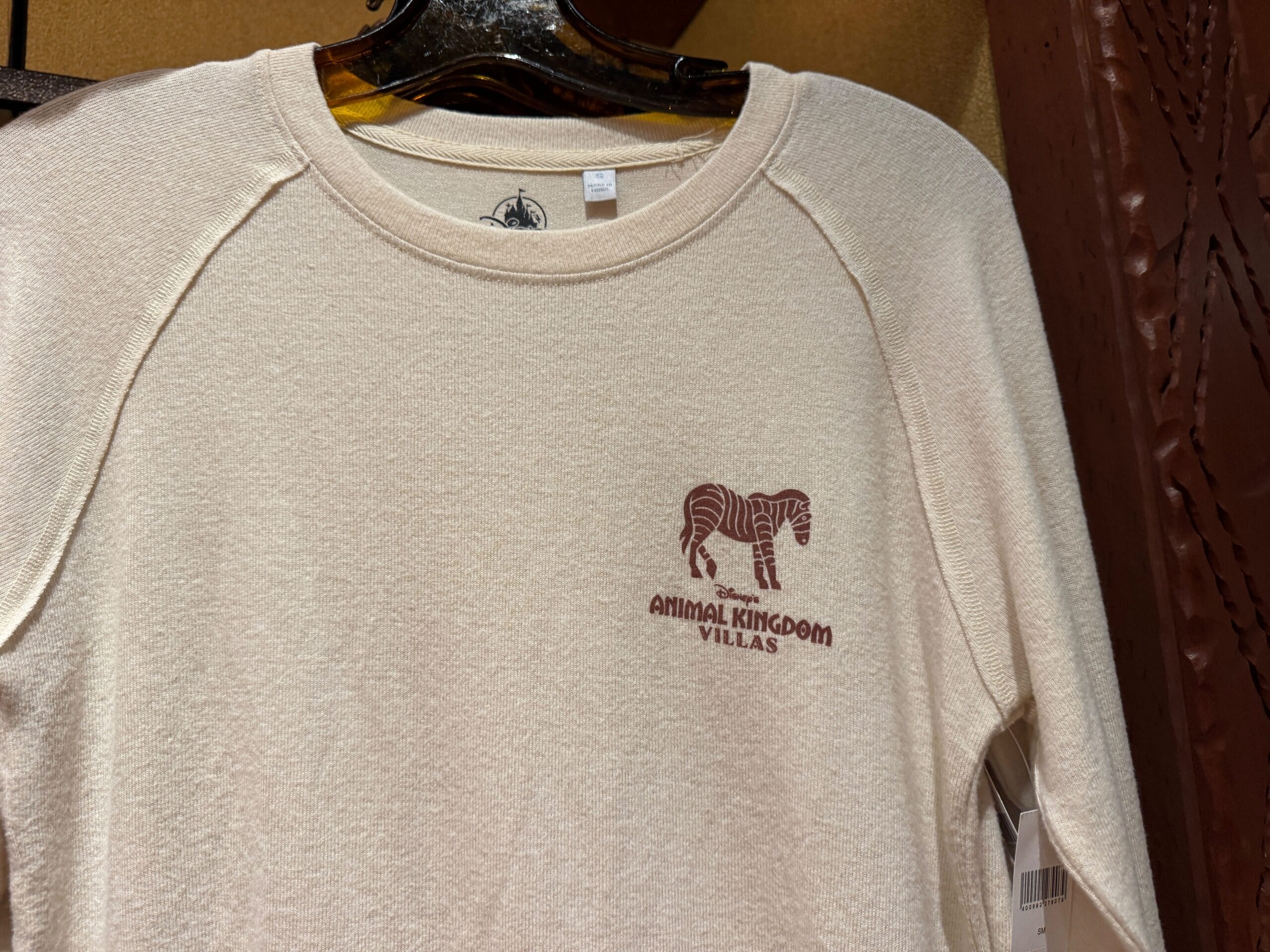 Cream sweatshirt with a maroon zebra graphic and "Animal Kingdom Villas" text on the upper left chest.