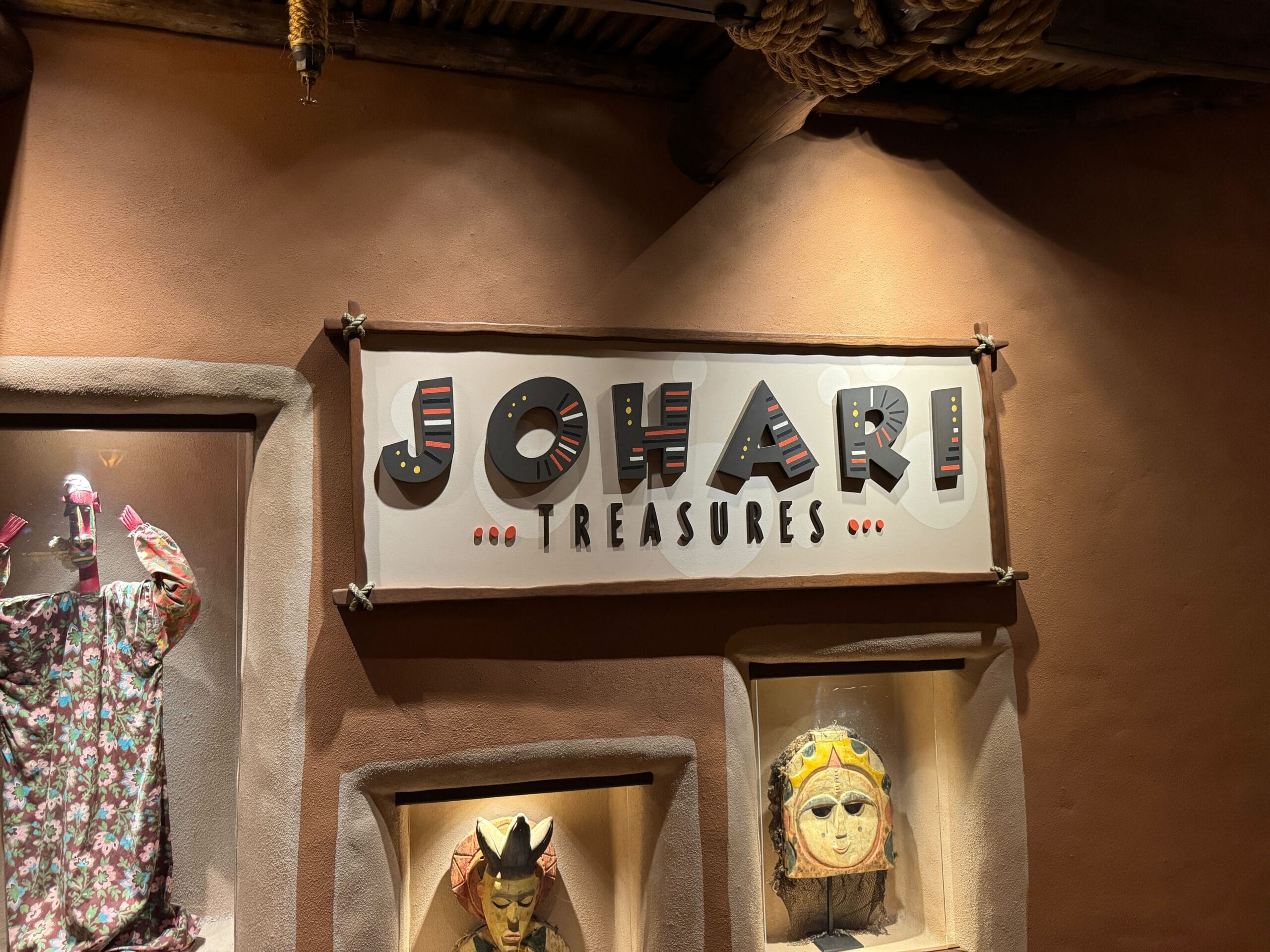 A sign reading "JOHARI TREASURES" is displayed above masks and a colorful garment in a dimly lit setting.