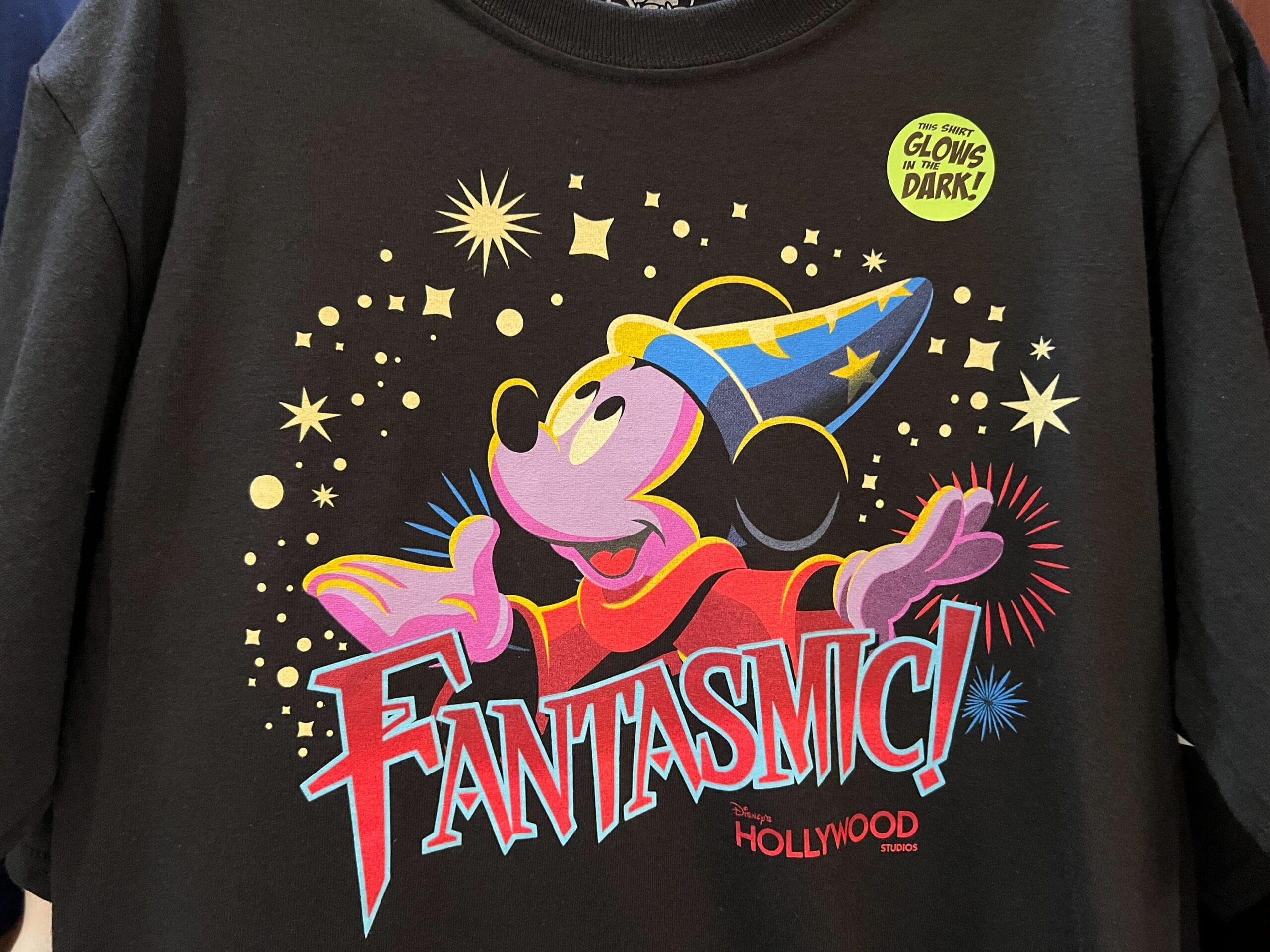 Fantasmic T-shirt with Sorcerer Mickey, stars, and a "Glows in the Dark!" sticker from Disney's Hollywood Studios.