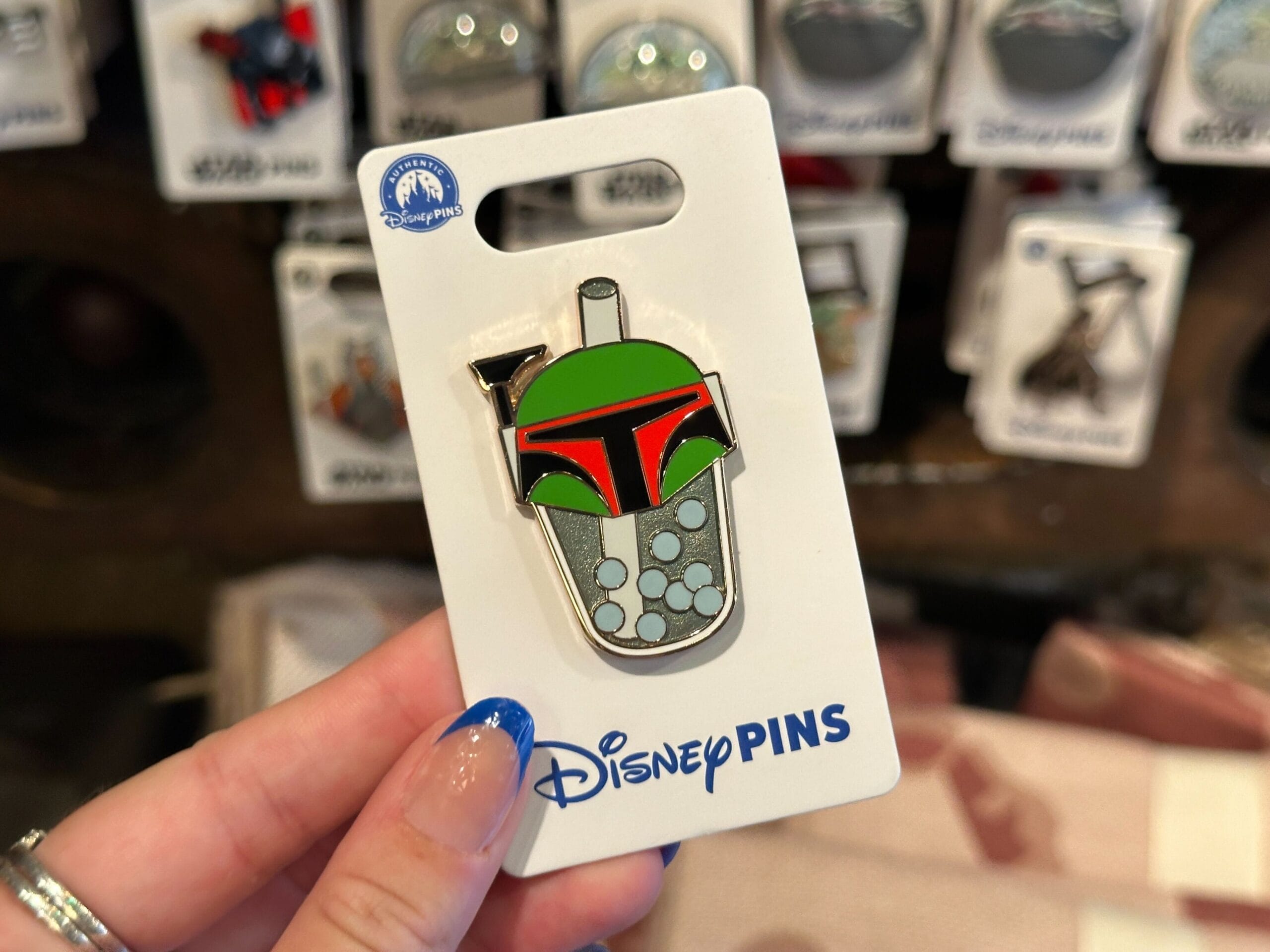 A hand holds a Disney Boba Fett bubble tea pin, with Star Wars pins blurred in the background.
