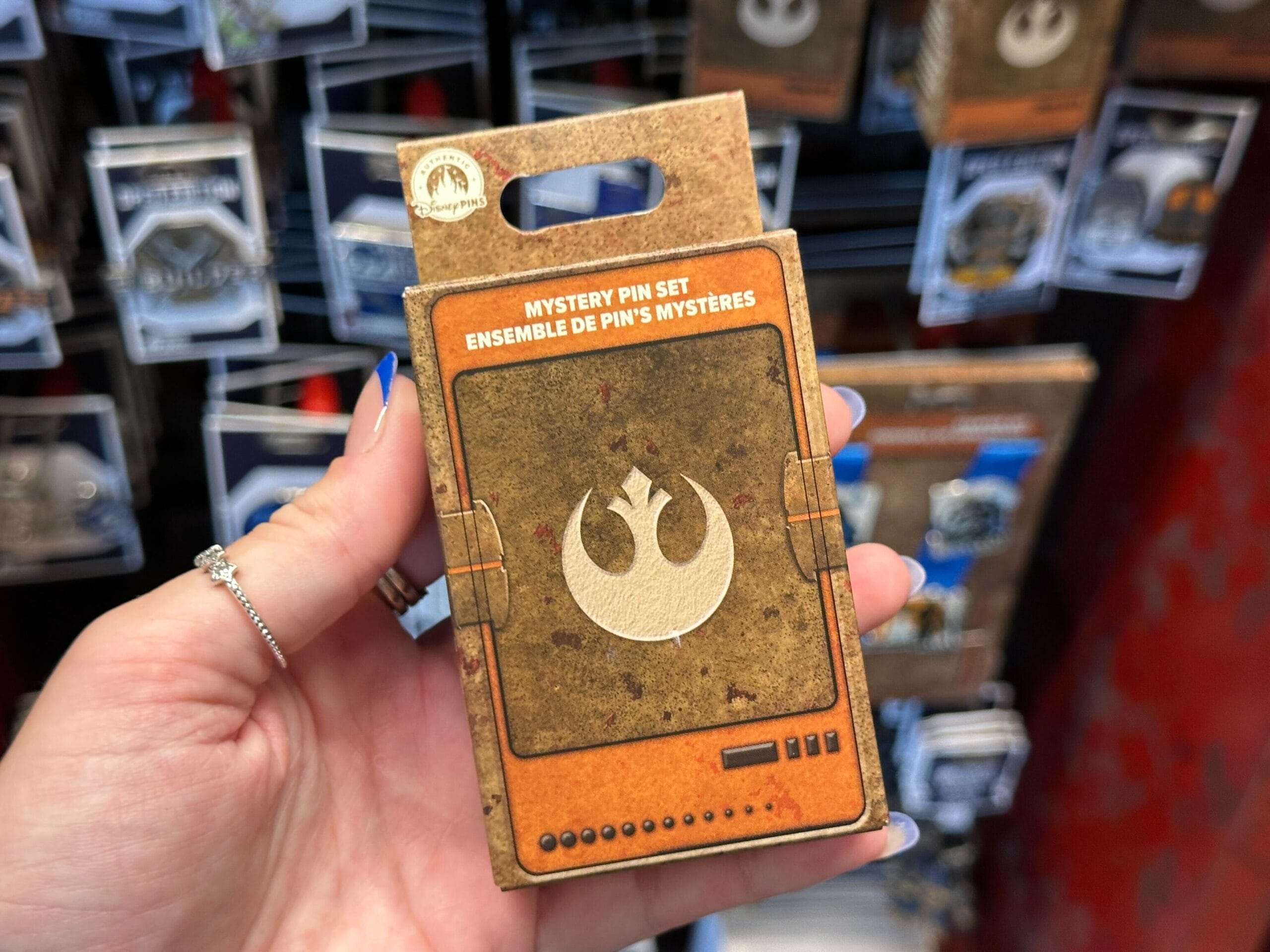 A hand holds a Star Wars-themed mystery pin set box from Walt Disney World featuring the Rebel Alliance symbol.