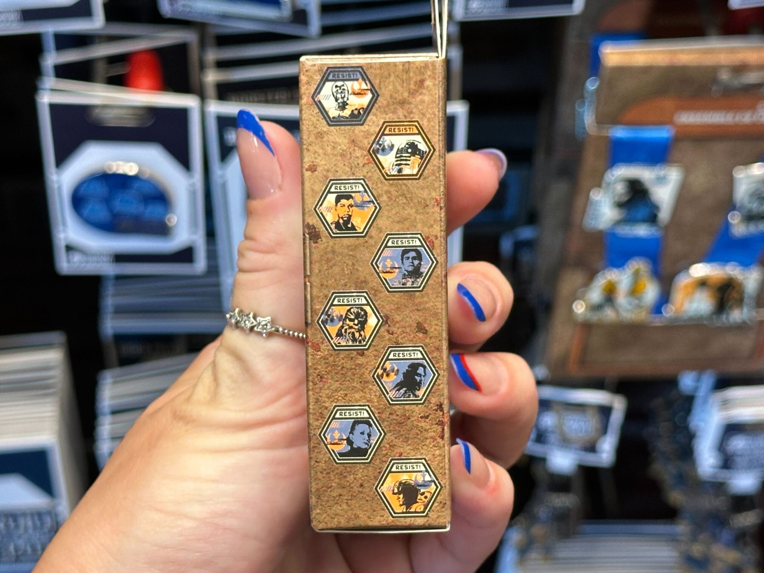 A hand with blue and orange nails holds a hexagonal Star Wars pin set featuring Boba Fett and other characters.