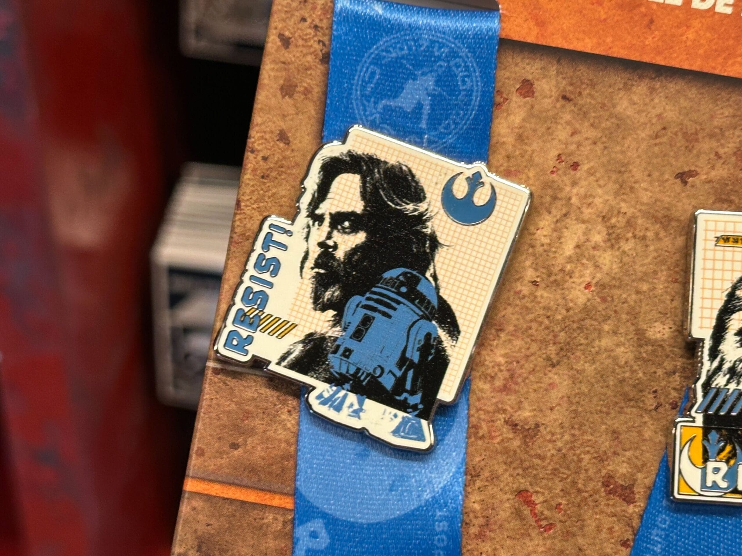 A Star Wars pin showing Luke, R2-D2, "RESIST!", and the Rebel Alliance symbol on a Walt Disney World display card.