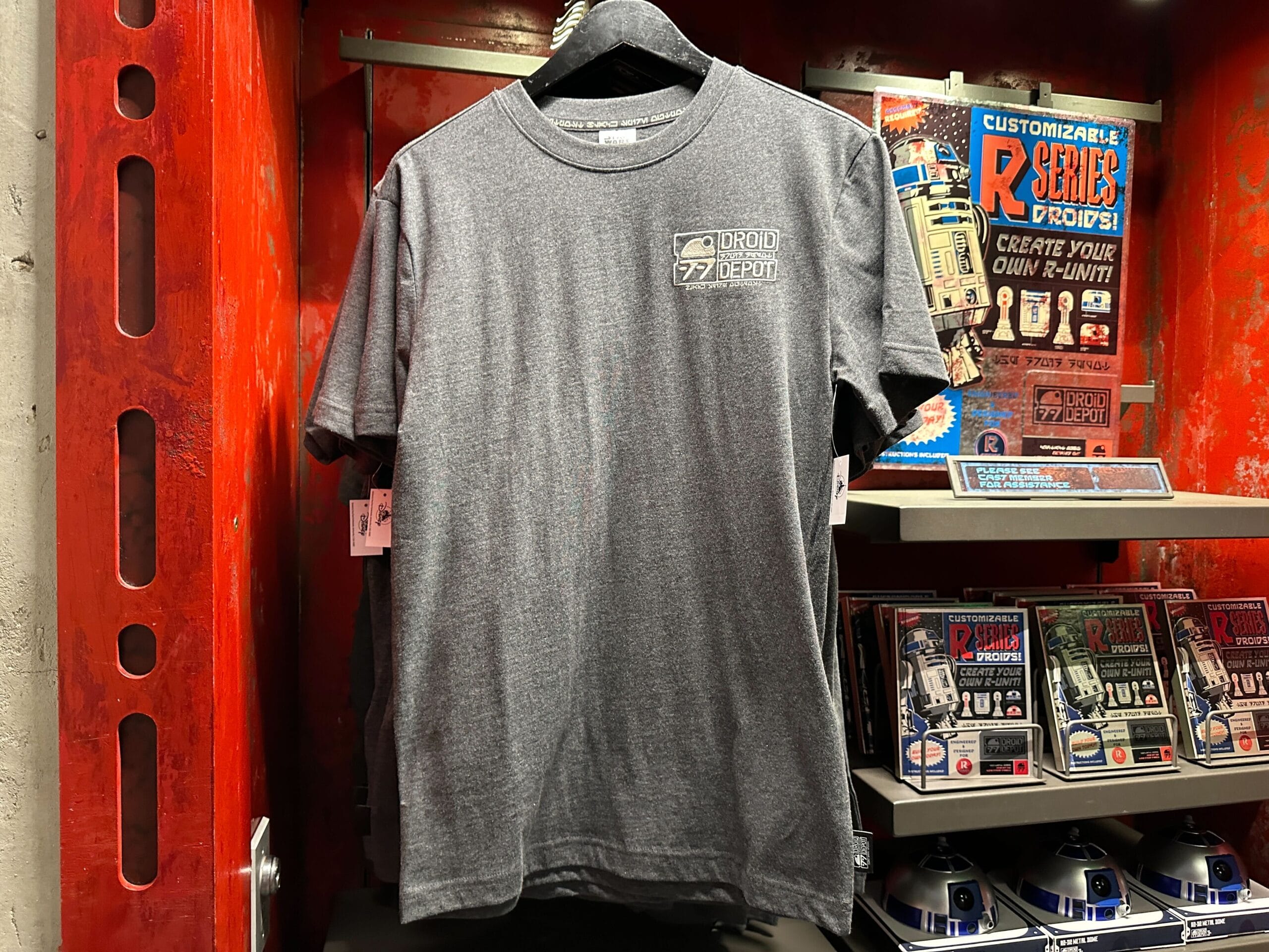 Gray "Droid Depot" t-shirt on display in a store with Star Wars merchandise and R2-D2 models in the background.