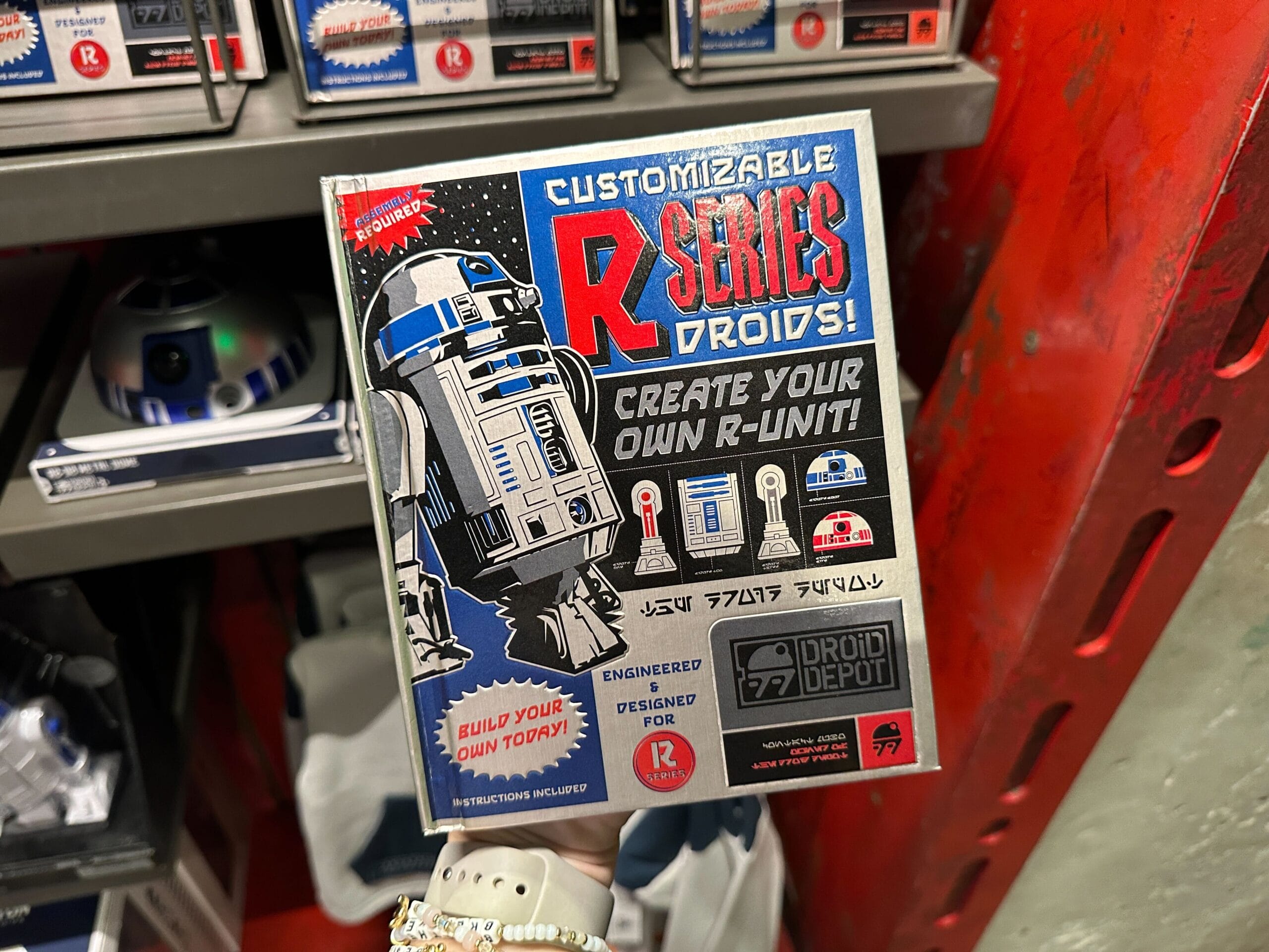 A hand holds a "Customizable R-Series Droids" box featuring an R2-D2 style robot and Star Wars-themed text.