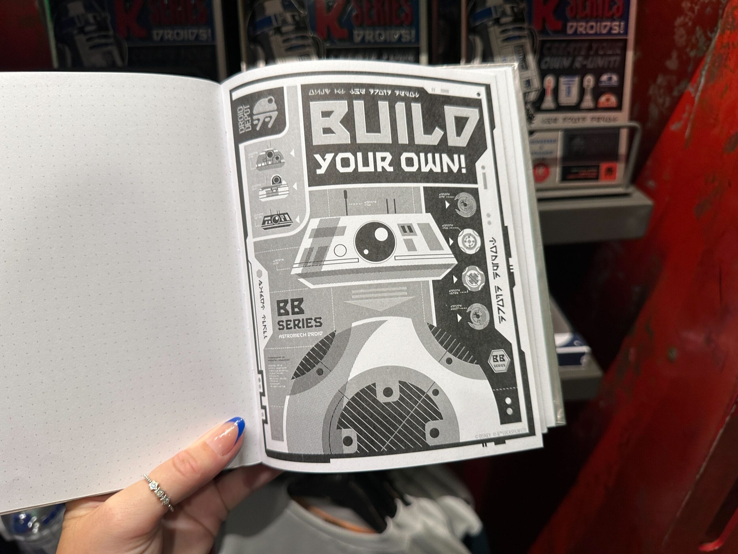 A hand holds open a booklet displaying a "Build Your Own BB-Series Droid" diagram in black and white.