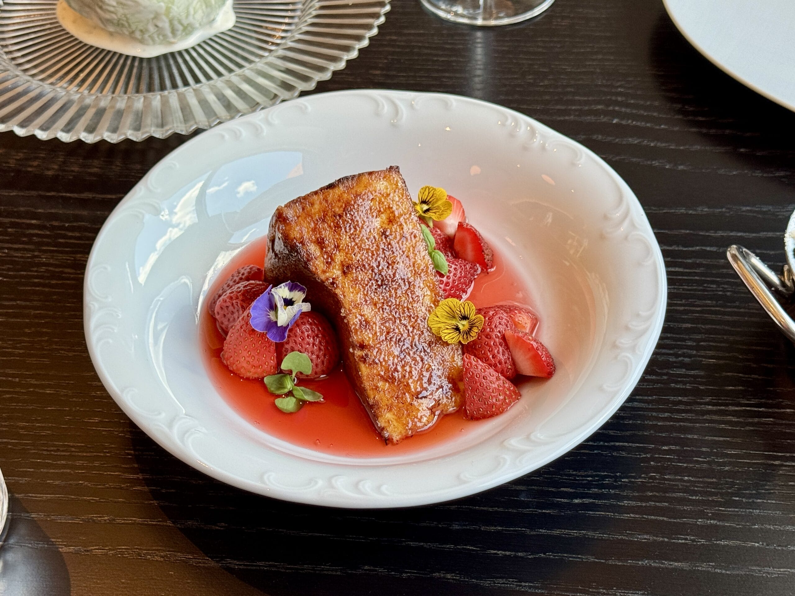 A caramelized dessert at Bourbon Steak, served with strawberries and edible flowers in a white bowl on a dark table.