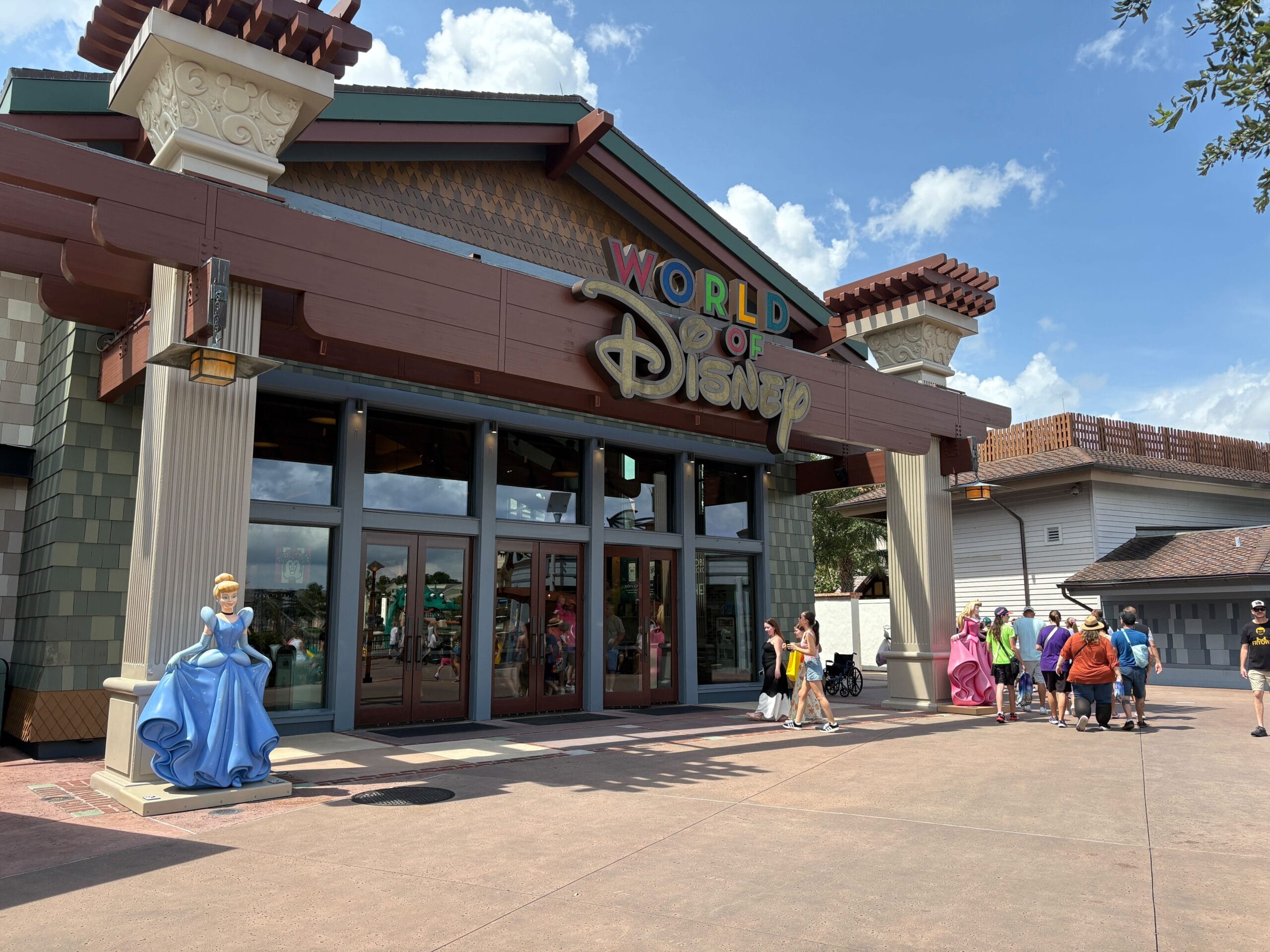Entrance to the Disney Springs World of Disney store with Cinderella Statue and people enjoying a sunny day.