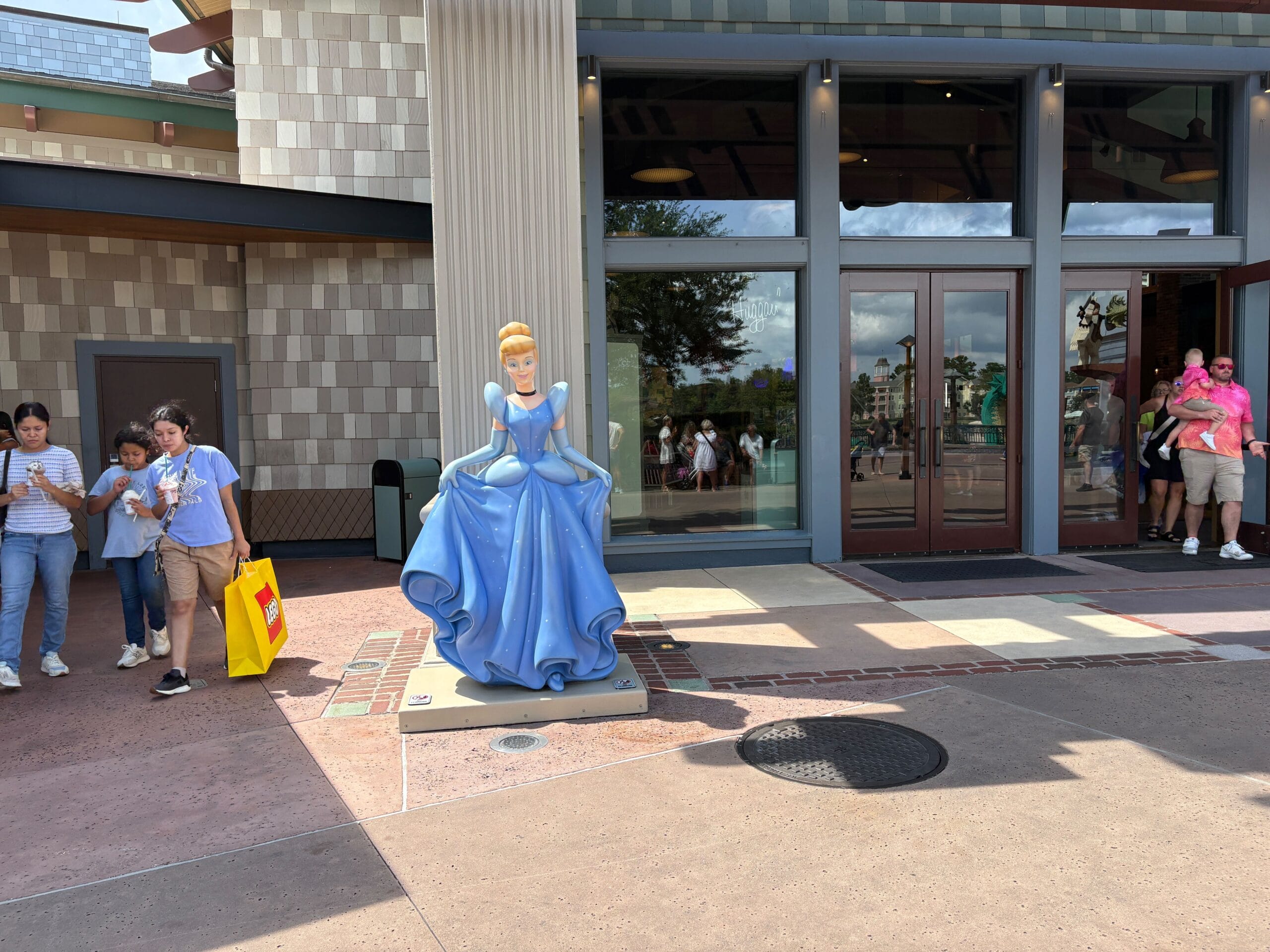 A Cinderella Statue stands outside World of Disney in Disney Springs as people walk and stand nearby on a sunny day.