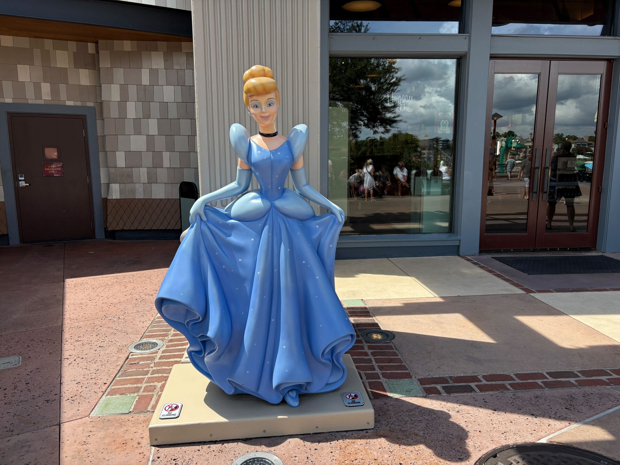 A Cinderella Statue in a blue gown stands outside World of Disney at Disney Springs on a sunny day.