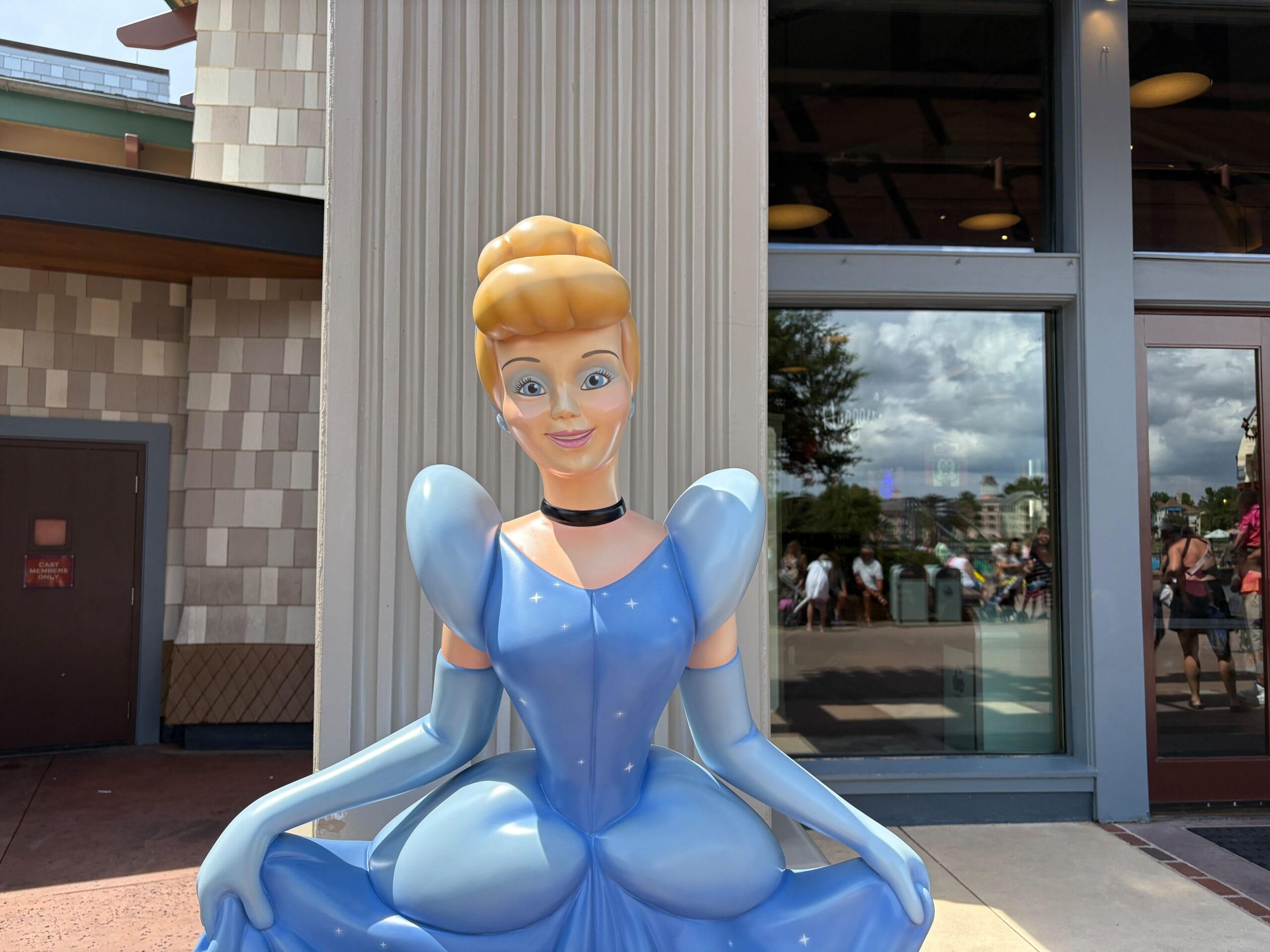 A life-sized Cinderella Statue in a blue dress stands outside the large windows of World of Disney in Disney Springs.
