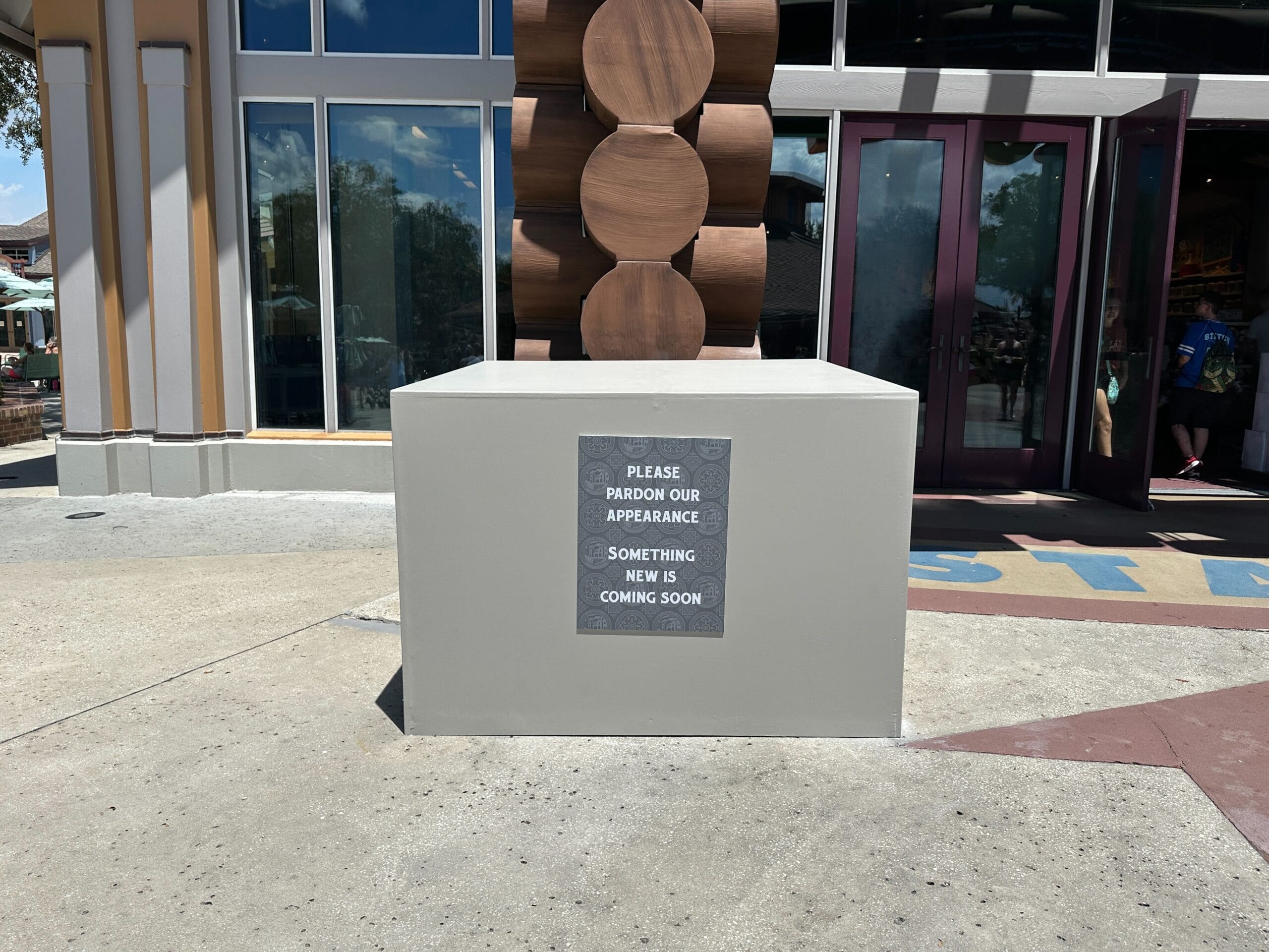 A gray box with a sign reads, "Please pardon our appearance. The missing statue at Disney Springs is coming soon.