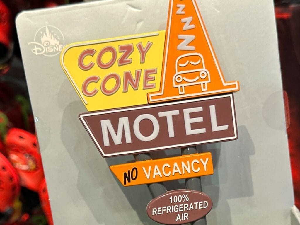 Hand holding a “Cozy Cone Motel” light-up sign from Disney’s Cars, displayed near Cars-themed merchandise.