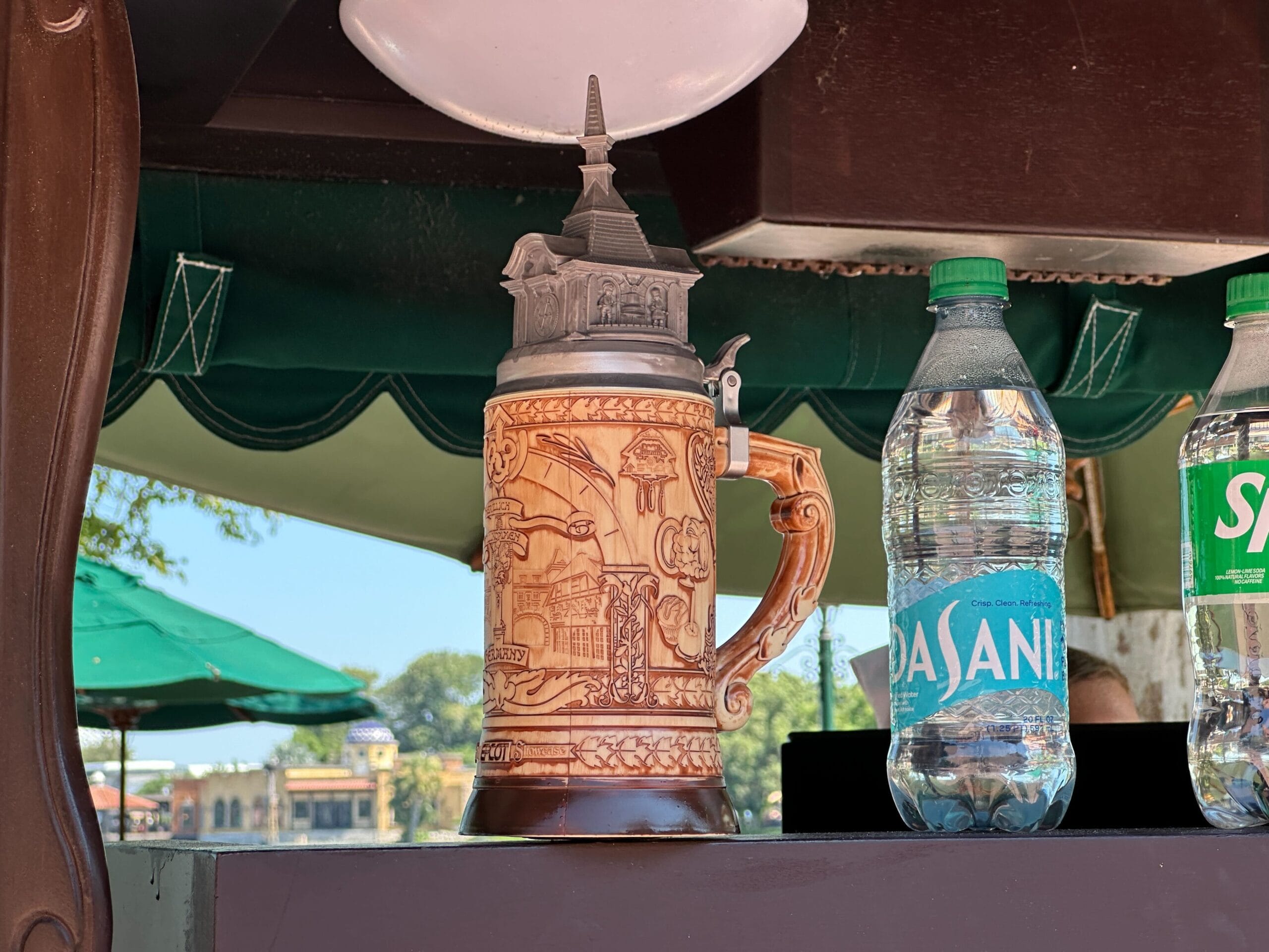 A decorative beer stein with a detailed design sits between two water bottles on a counter outdoors.