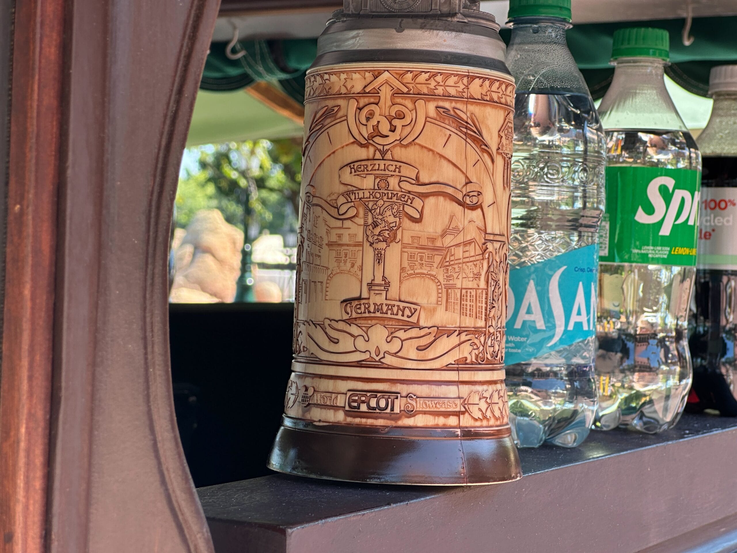 A decorative German beer stein sits on a shelf next to Dasani and Sprite water bottles.