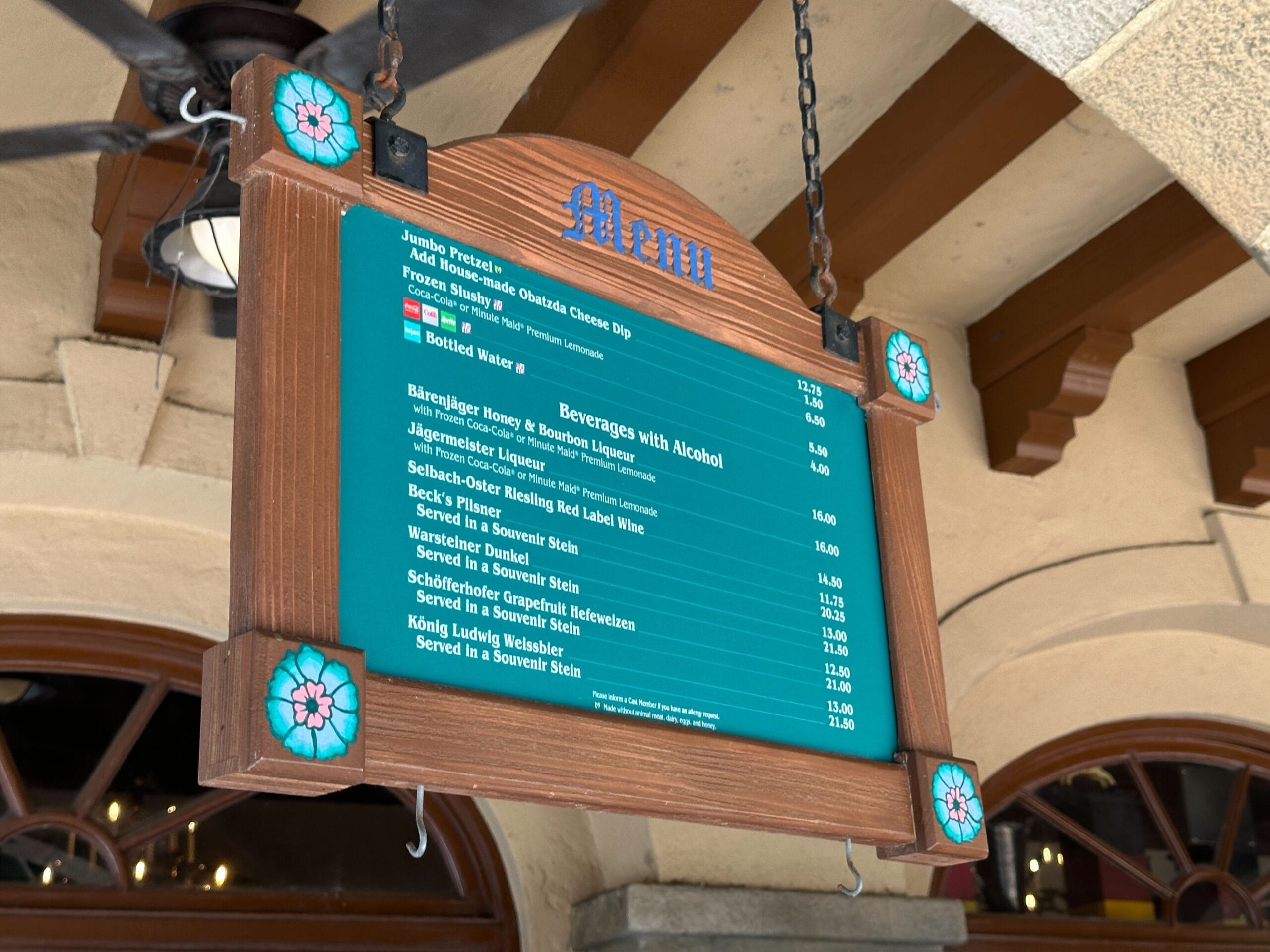 Wooden menu board with blue text displaying food and drink options, hanging from a ceiling with wooden beams.