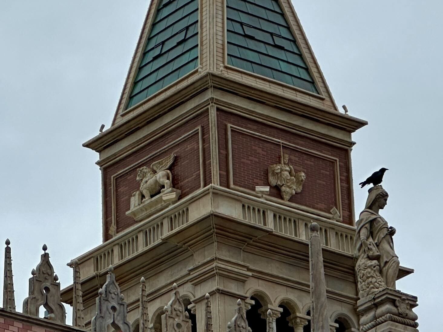 A crow perches on a statue atop a gothic-style building with ornate stonework and a pointed roof.