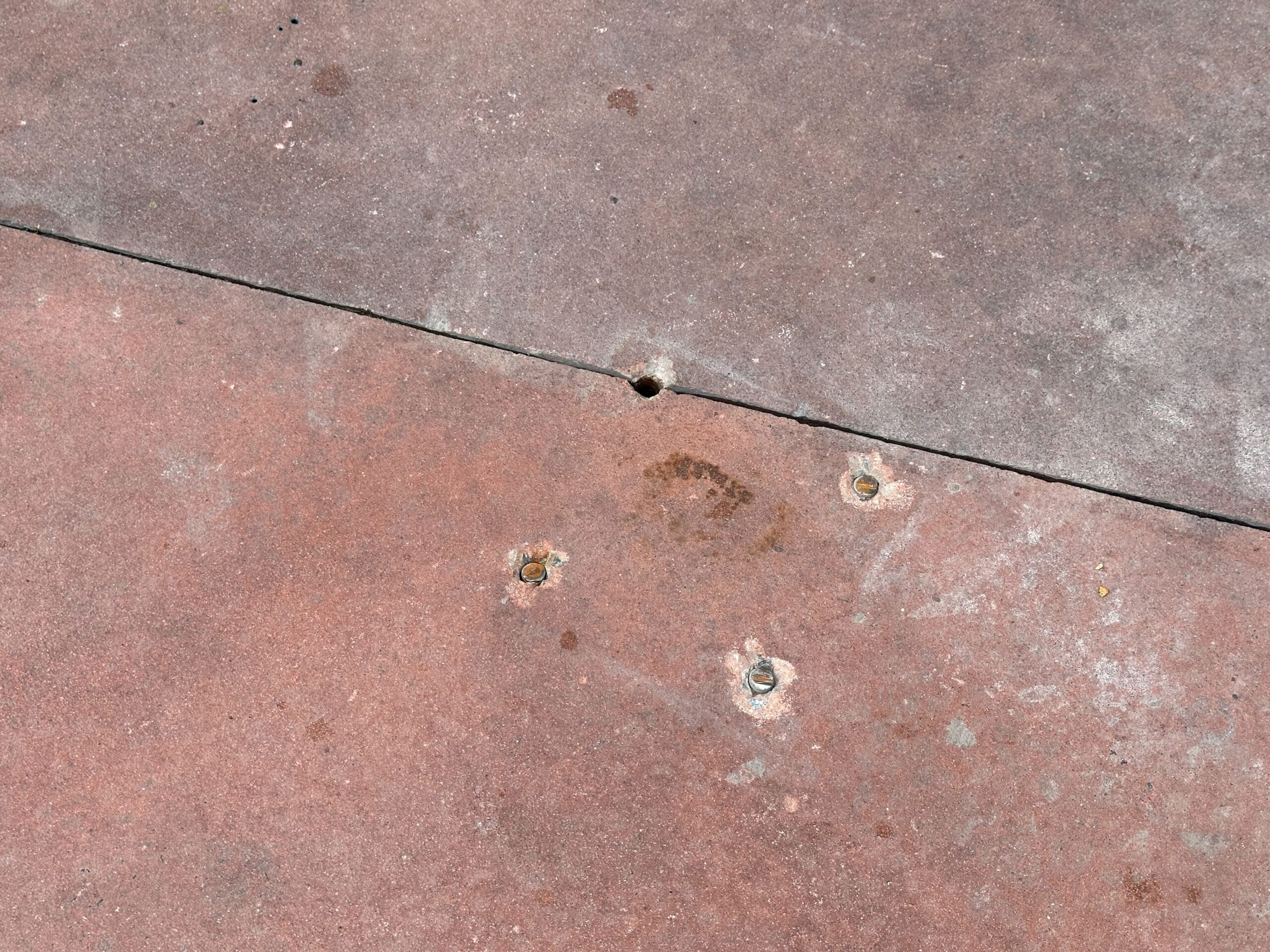Concrete surface with four old bolt holes, some with rust stains, and a visible seam running diagonally.