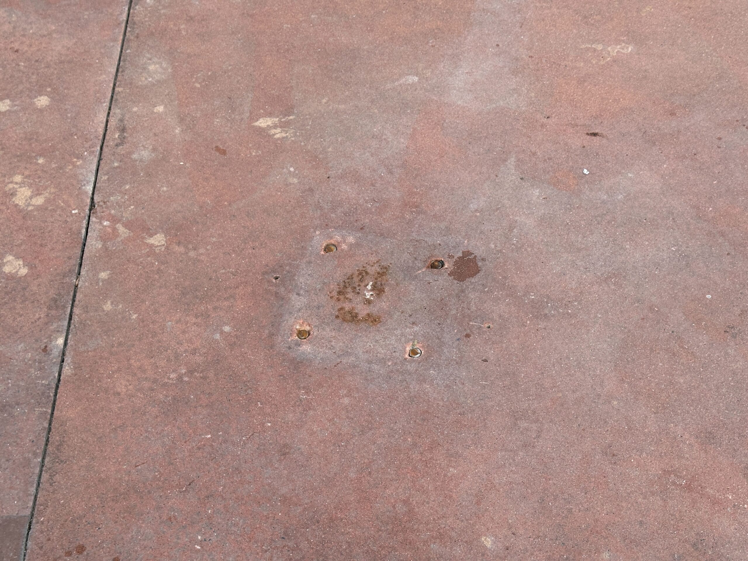 Rusty bolt holes and stains on a reddish-brown concrete surface with a visible seam on the left.