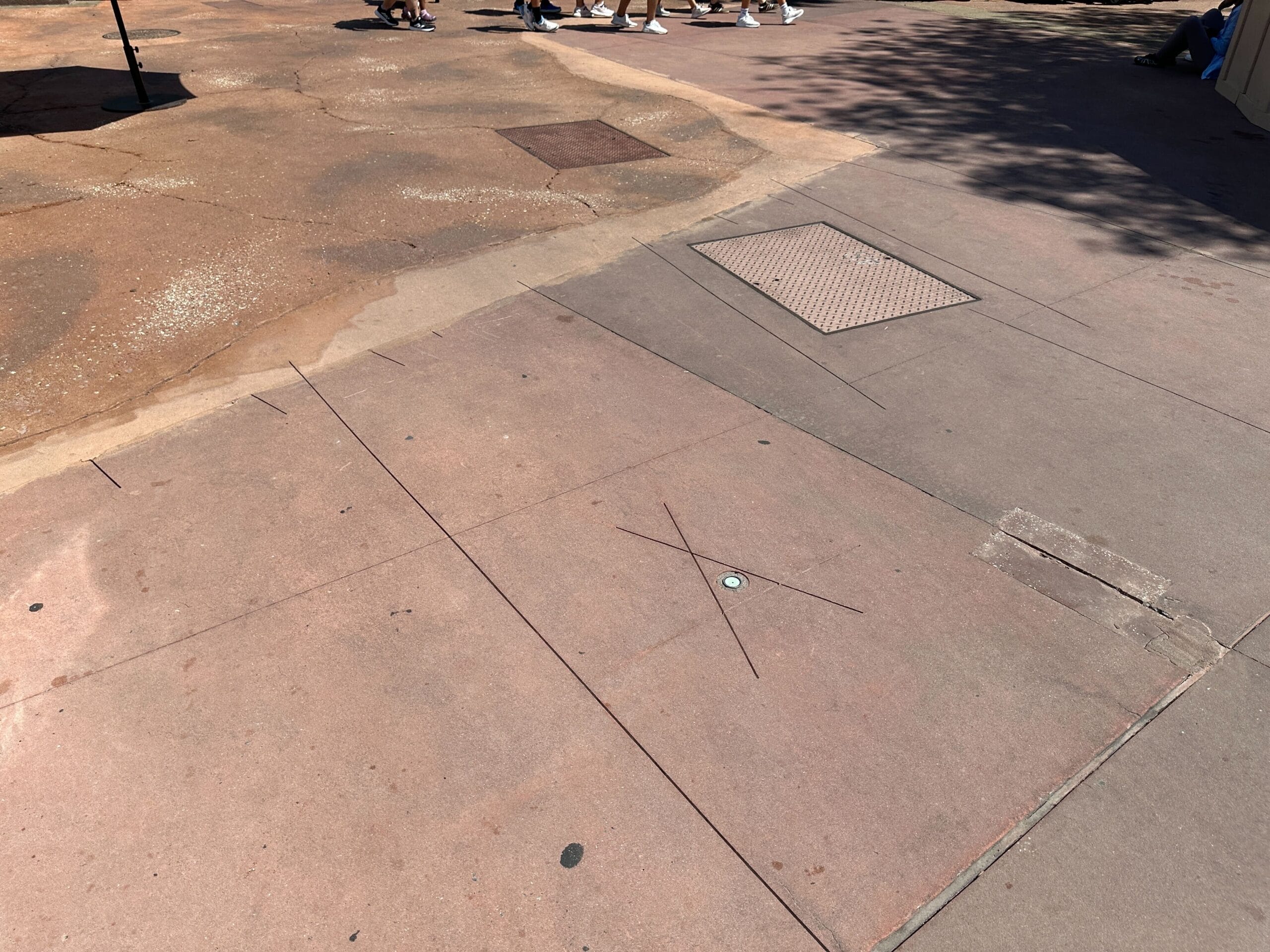 A sidewalk with a large X marked on it; people’s feet are visible in the background.