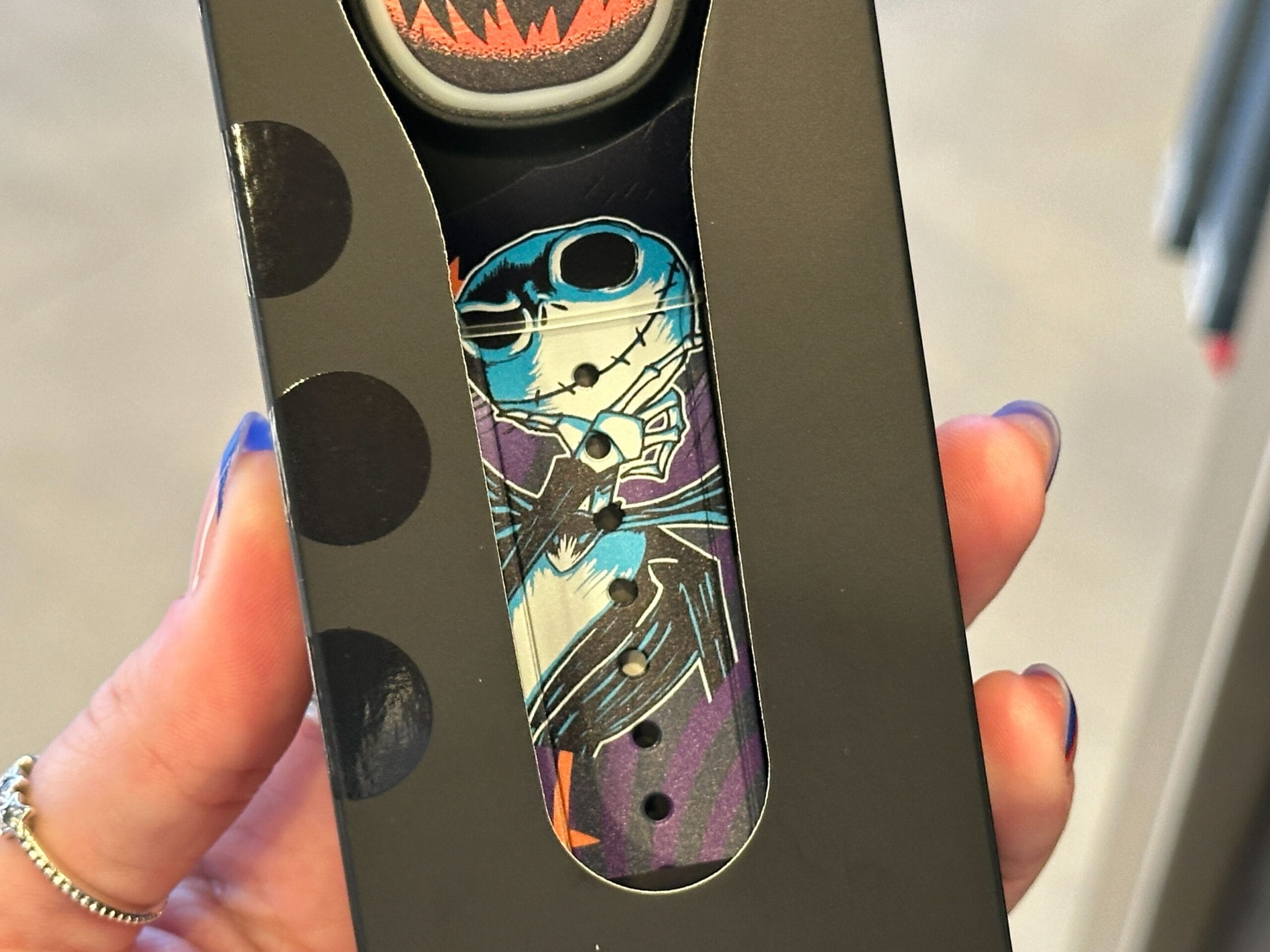 A hand holds a box revealing a MagicBand+ with a Jack Skellington design from Nightmare Before Christmas at EPCOT.
