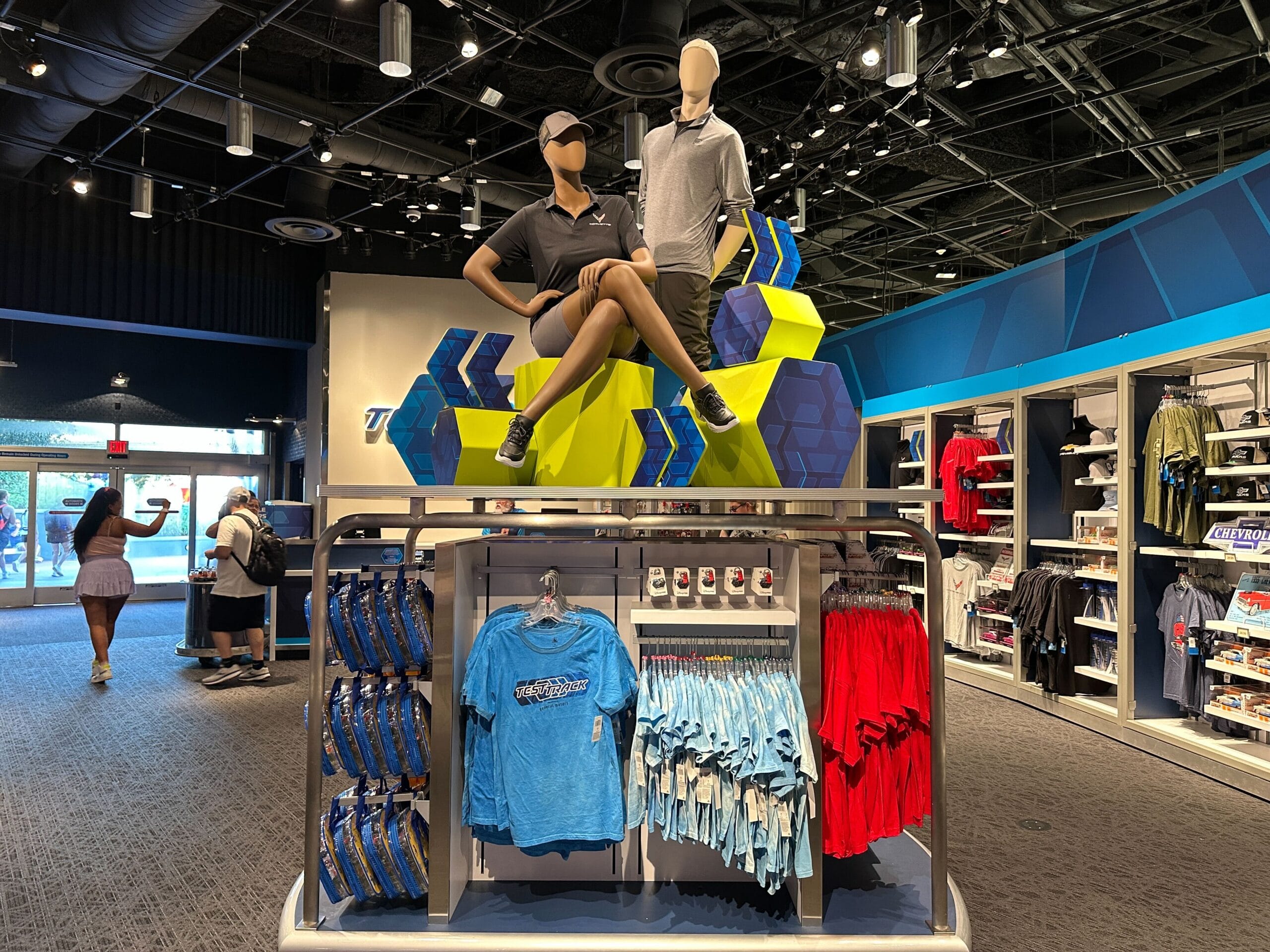 Retail store display with mannequins on a platform, surrounded by shirts, hats, and merchandise on shelves and racks.