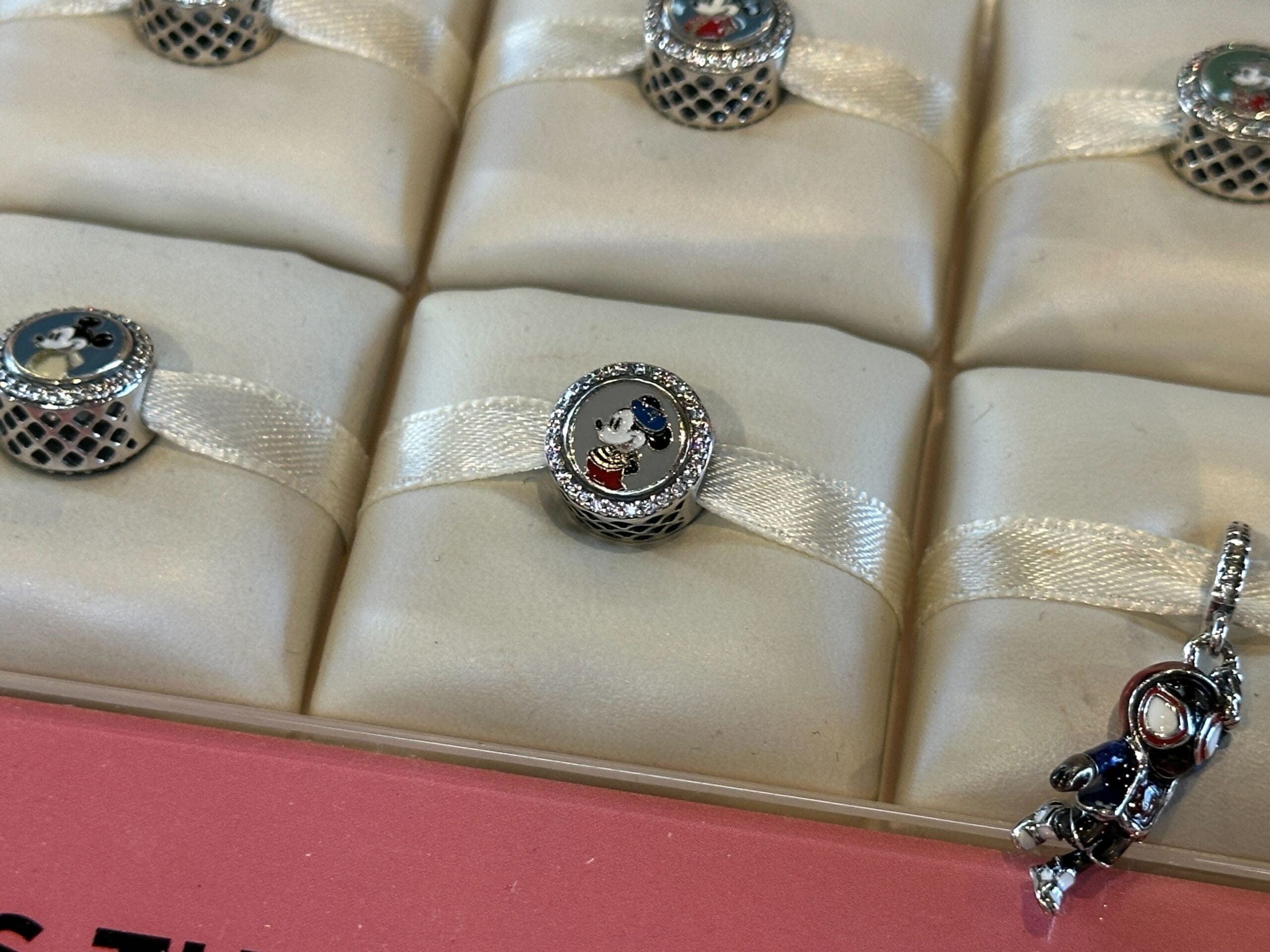 A silver and black oval charm displayed on a padded cushion, surrounded by similar jewelry pieces in a case.