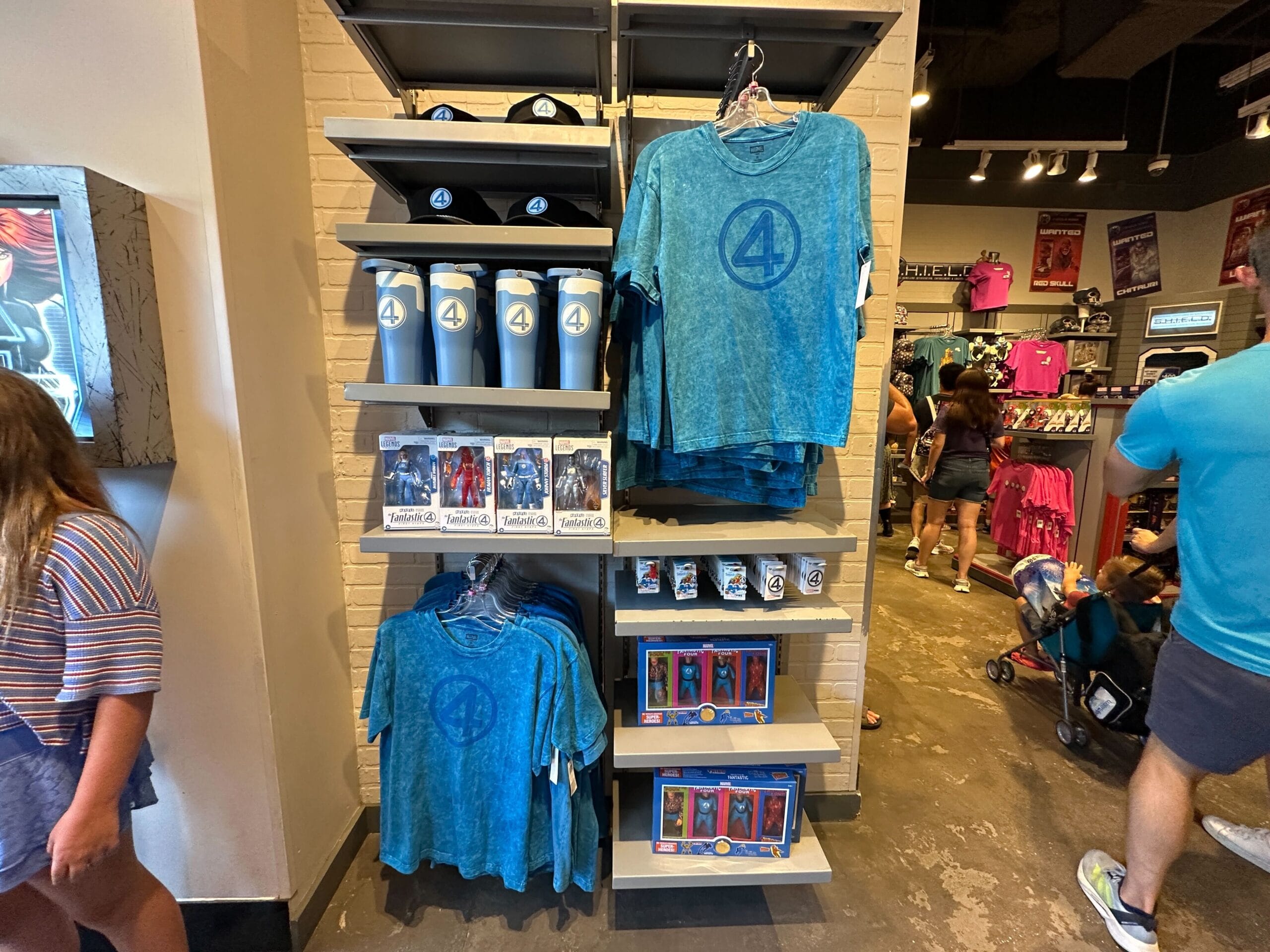 Display of Fantastic Four apparel and Marvel merchandise, like blue shirts, cups, hats, and action figures, in a store.