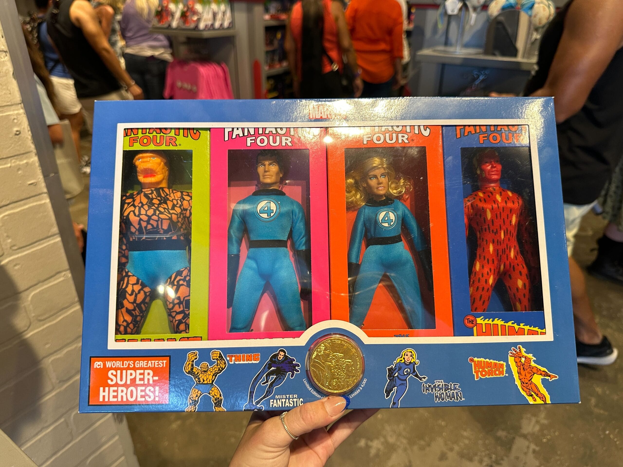 A hand holds a box of retro Fantastic Four action figures among Marvel merchandise in a store.