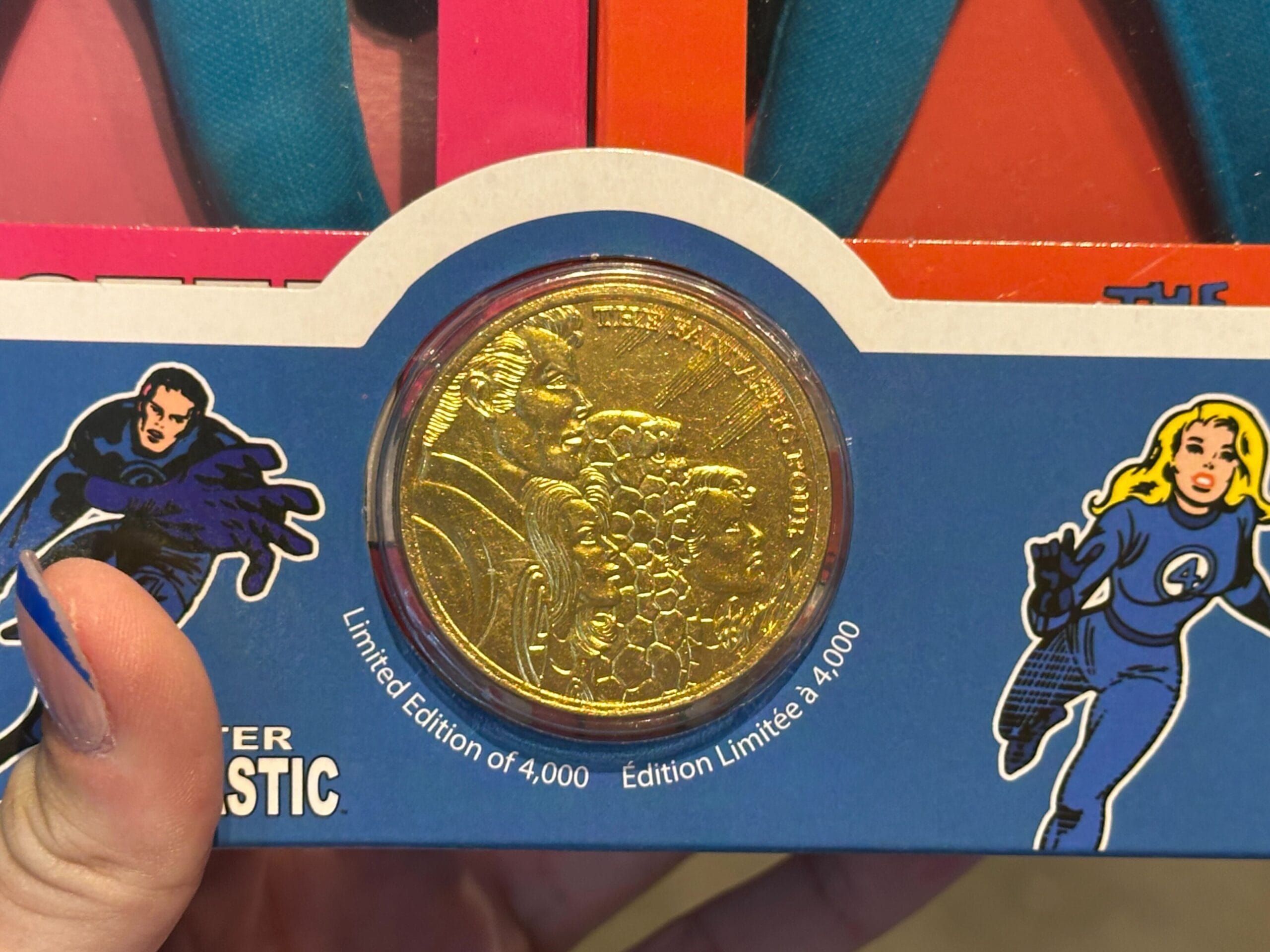 A gold coin labeled "Limited Edition of 4,000" held in front of Marvel merchandise featuring Fantastic Four.