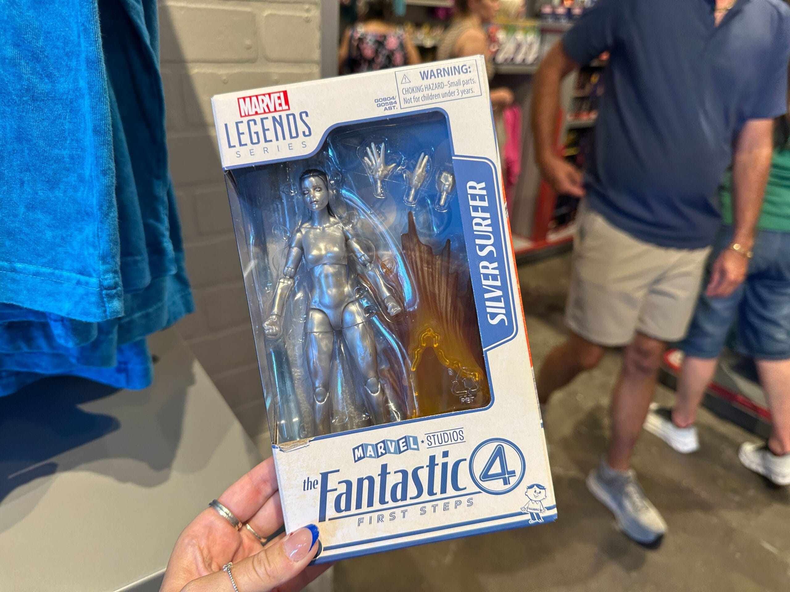 Hand holding a Marvel Legends Silver Surfer action figure in Fantastic Four packaging among Marvel merchandise in-store.