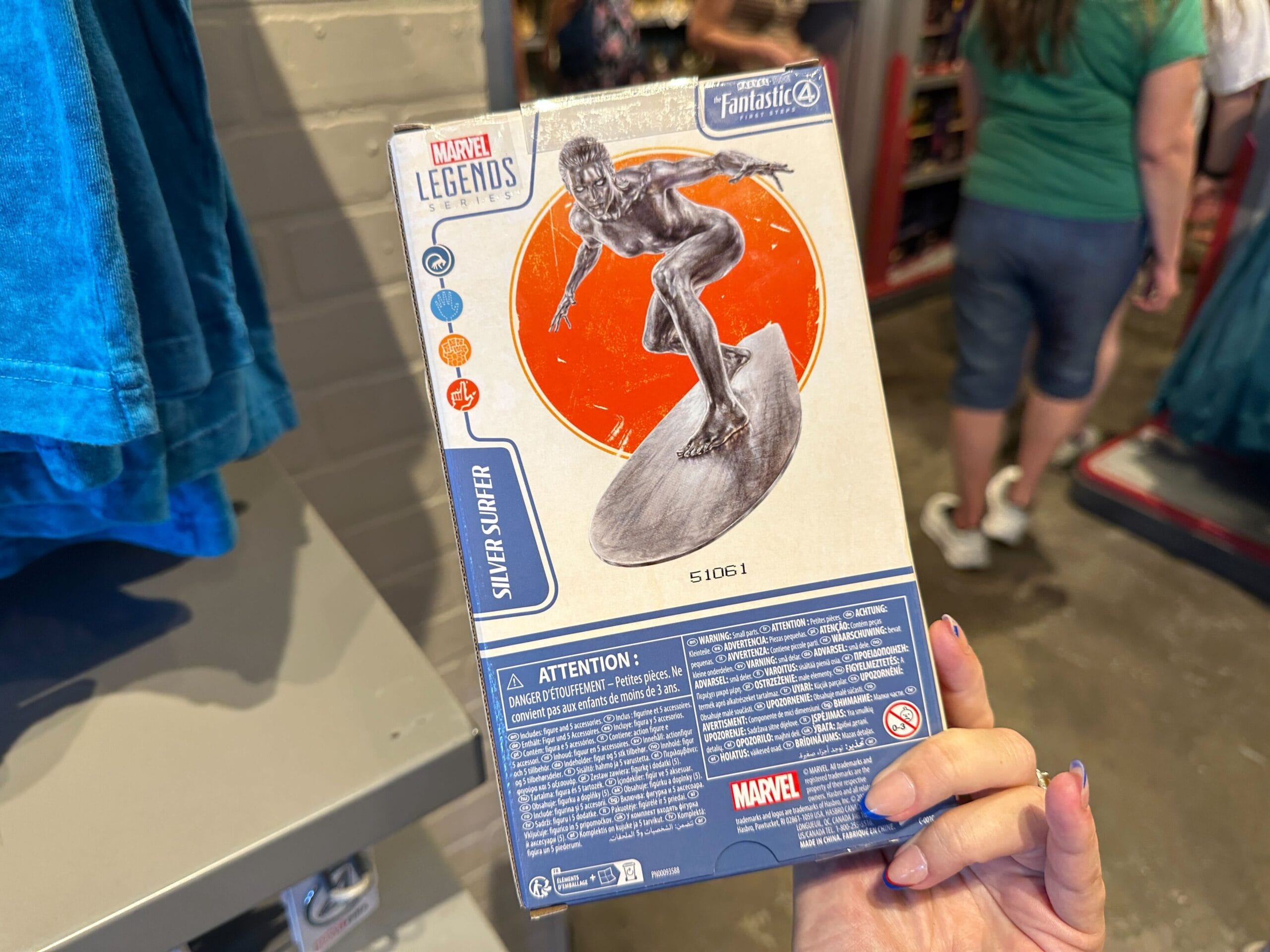 Person holding Marvel Legends Silver Surfer action figure box—perfect for Marvel merchandise fans—in a busy store.