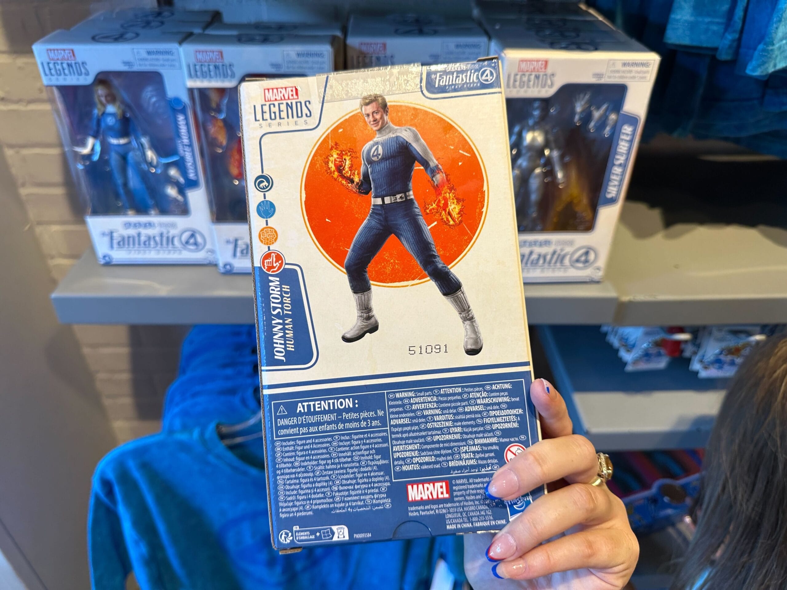 A hand holds a Marvel Legends Johnny Storm box, showcasing Marvel merchandise with fiery hands on the back.