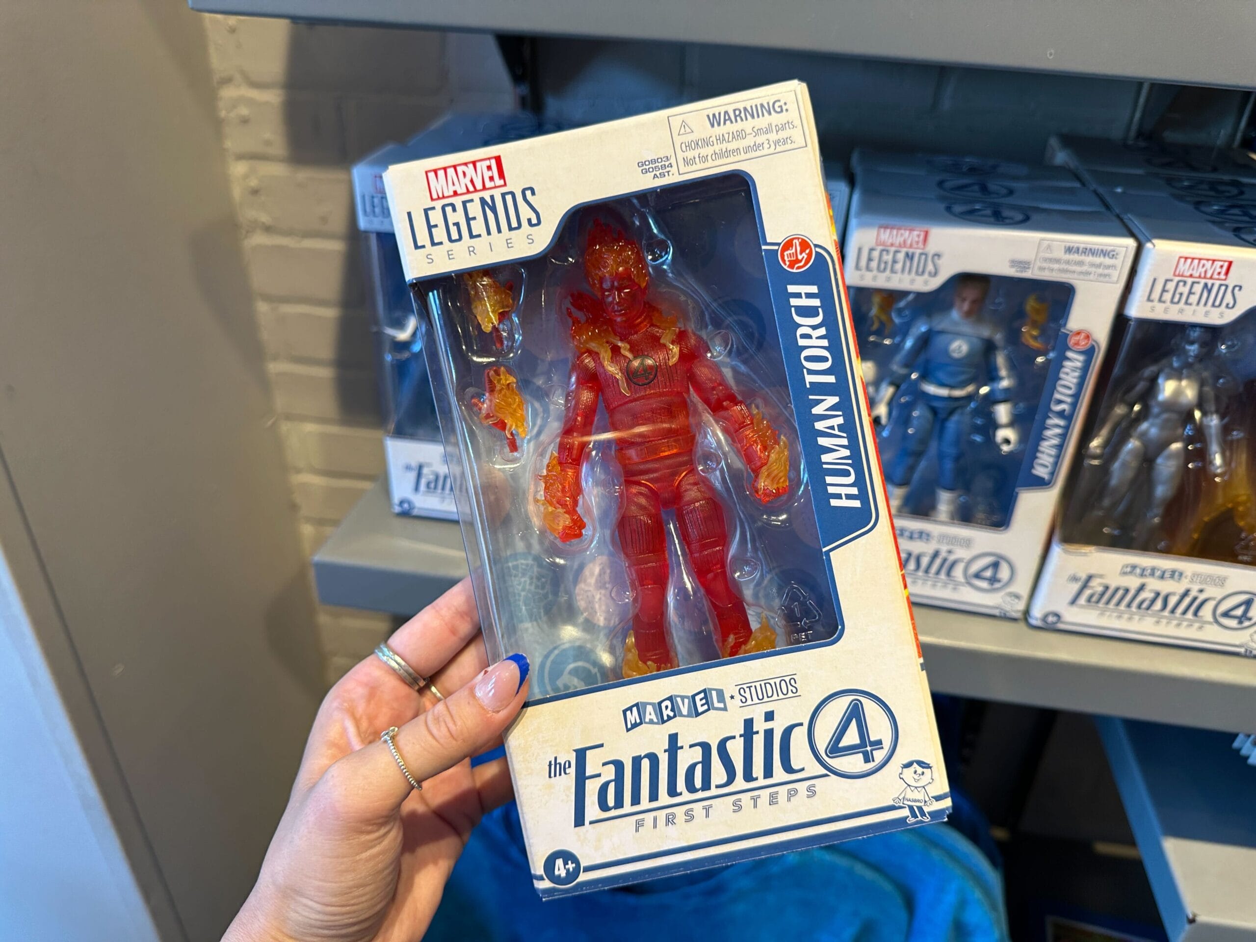 A hand holds Marvel merchandise—a Human Torch action figure in its box from The Fantastic Four First Steps series.