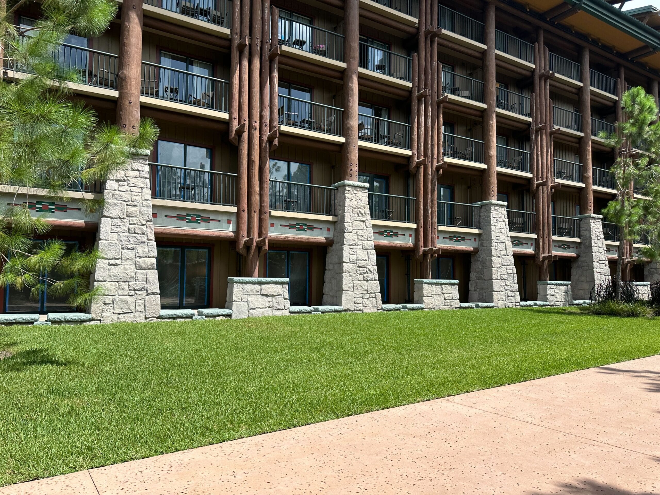 Ground level view of a lodge-style hotel building with balconies, stone pillars, and a green lawn in front.