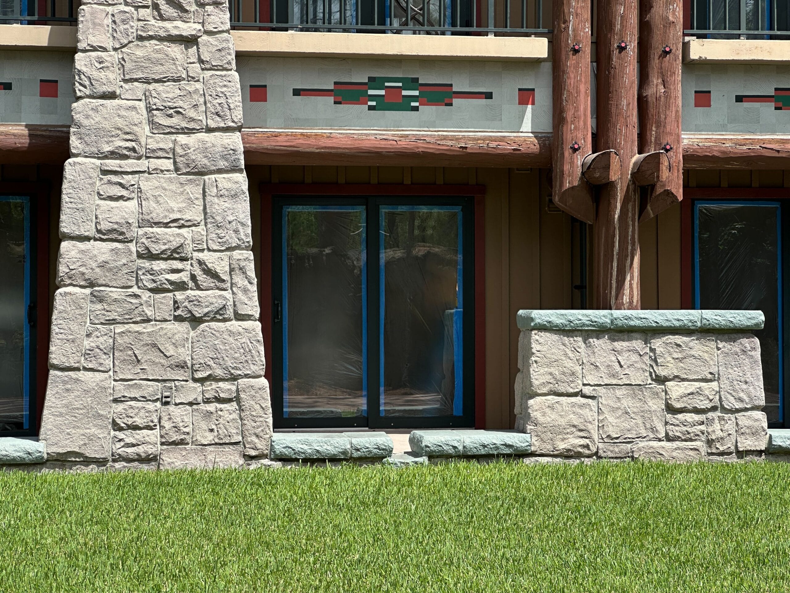 A stone patio with glass doors, wooden beams, and green grass in front of a building.