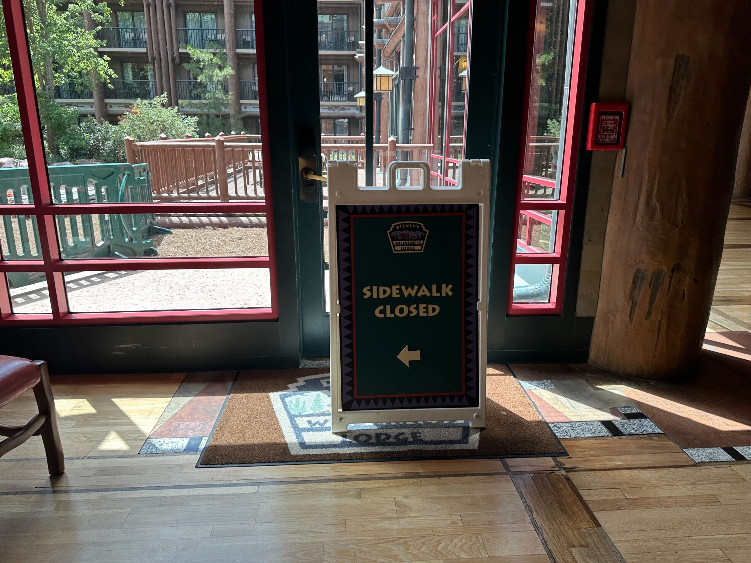 A sign inside a building reads "Sidewalk Closed" with a left arrow, blocking a glass door to the outside.