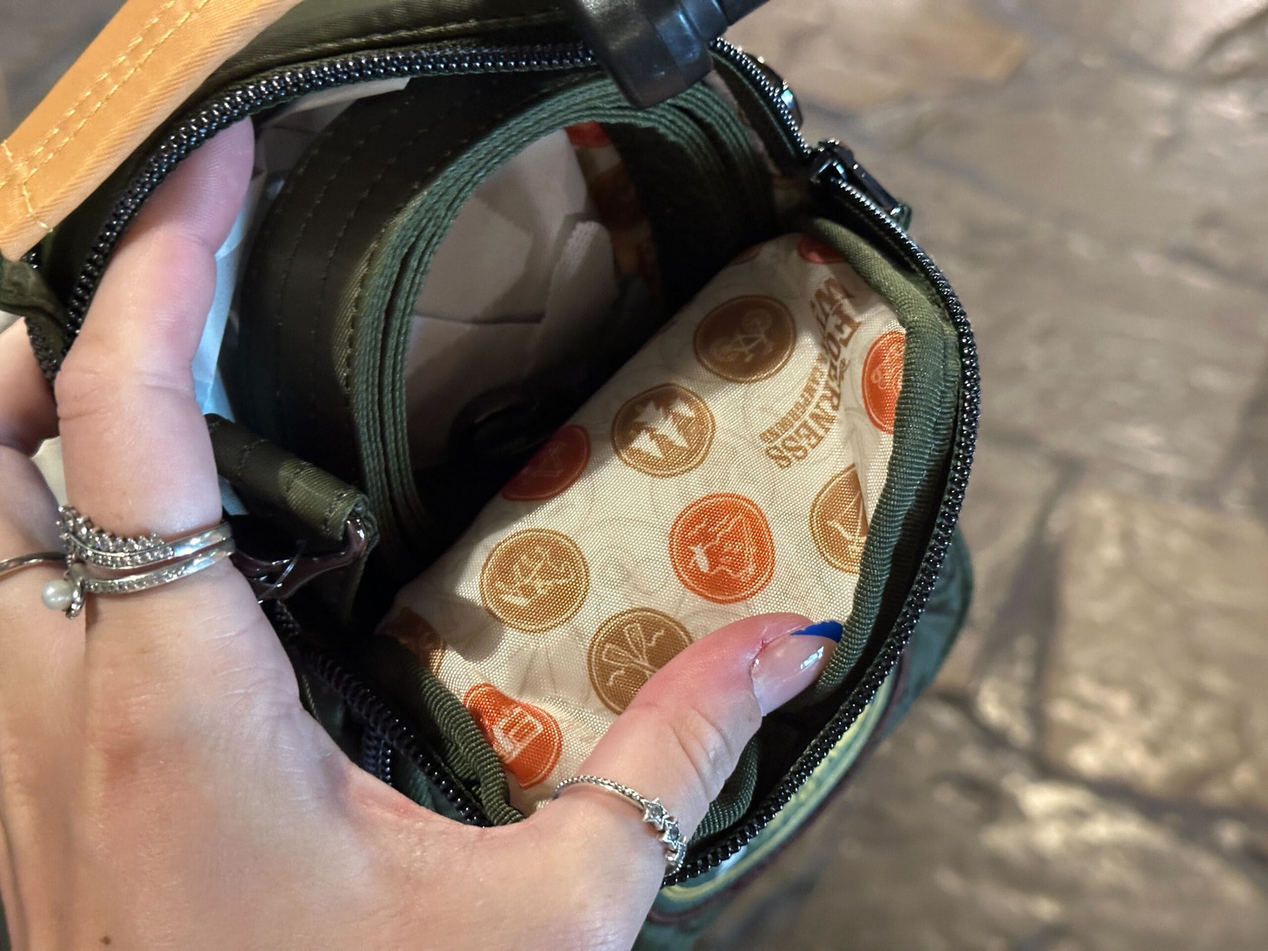 A hand opens a small green bag, showing patterned fabric with various circular logos inside.