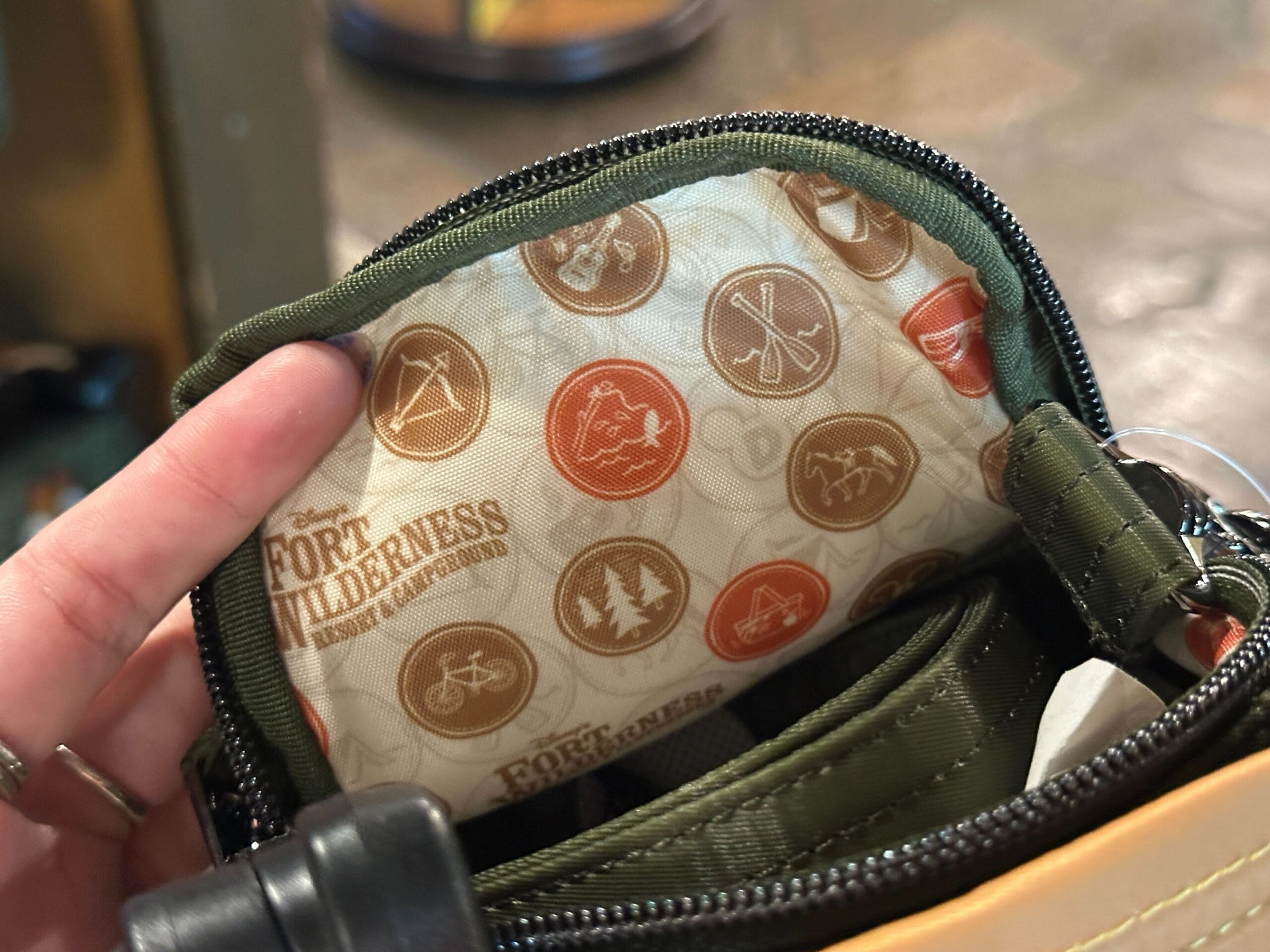 A hand holds open a small pouch with Fort Wilderness logo and camping-themed icons on the inside lining.