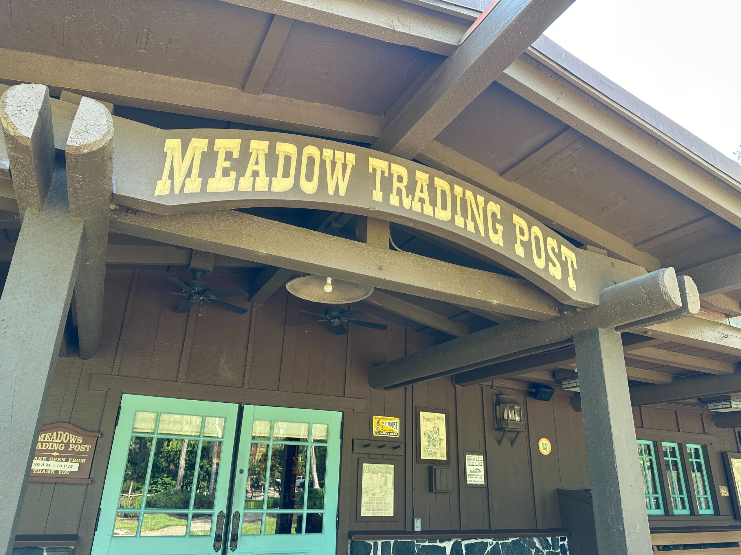 Rustic wooden Meadow Trading Post building with teal doors and a large sign above the entrance.