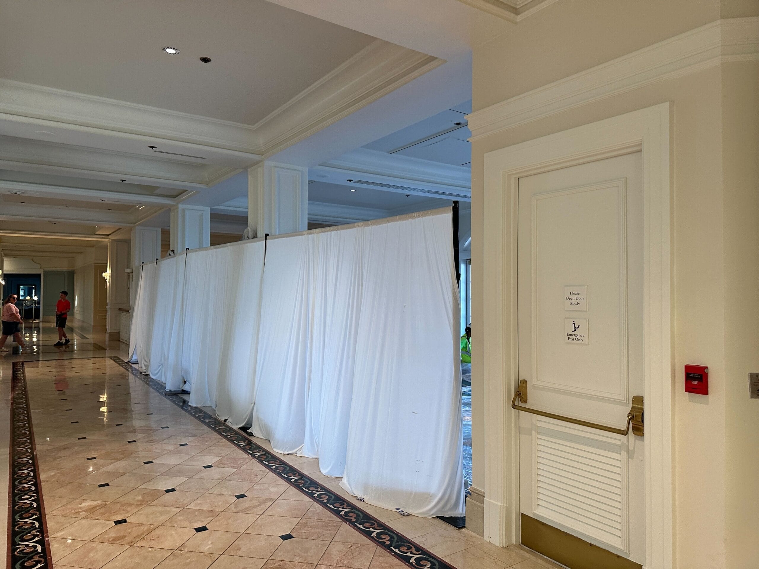 White curtains hang across a hallway in a hotel, partially blocking off an area. A few people stand in the distance.
