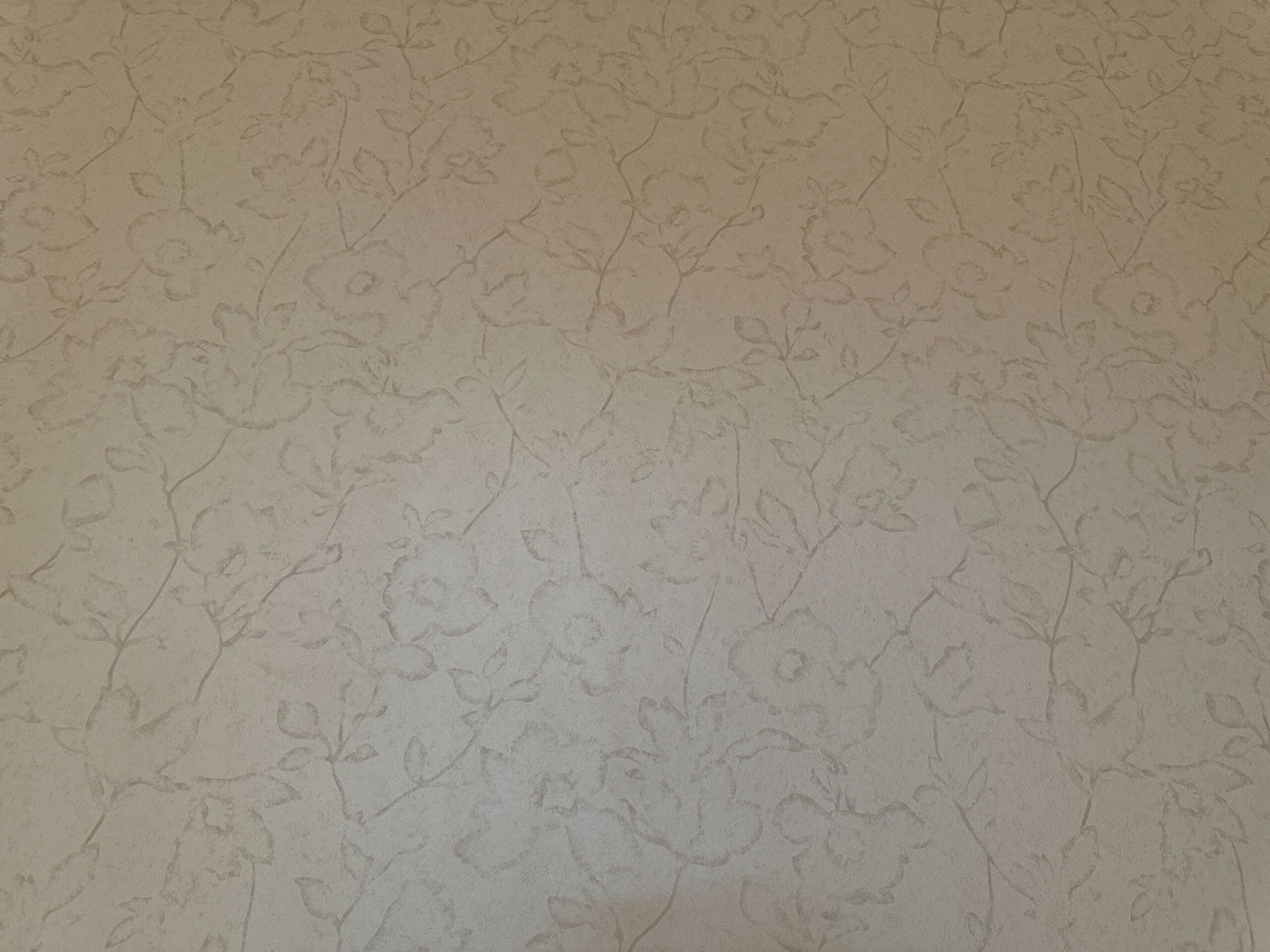 Beige wallpaper with a subtle floral and vine pattern in a raised, textured design.